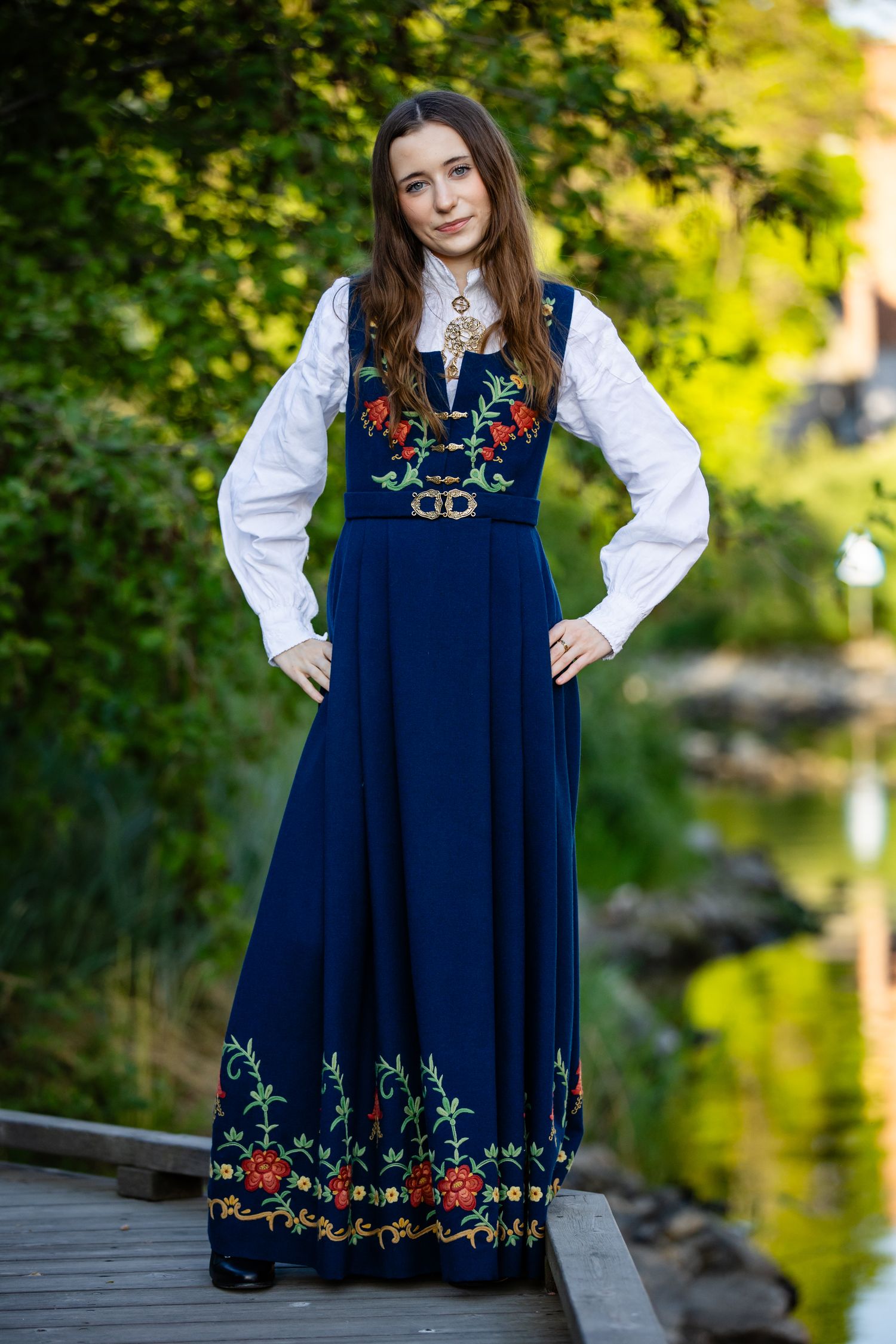 Person wearing navy blue dress with colorful embroidered details poses by waterside.