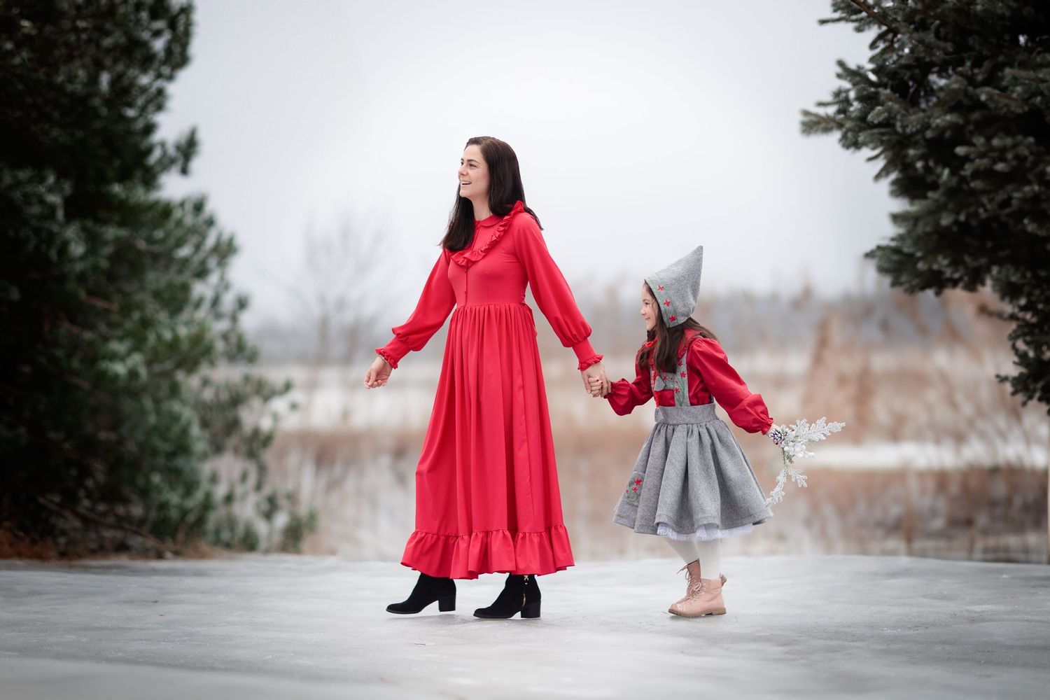 Mother and child in matching red dresses holding hands on icy surface in winter setting.