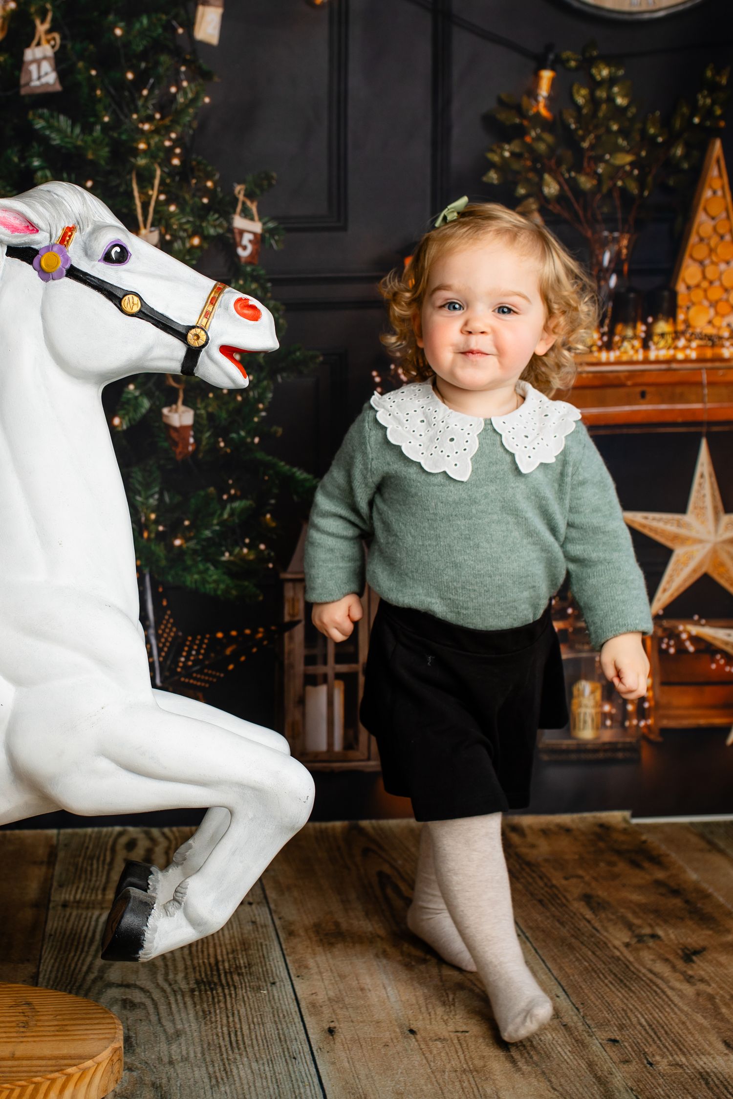 Decorative white carousel horse with festive Christmas backdrop and wooden flooring.