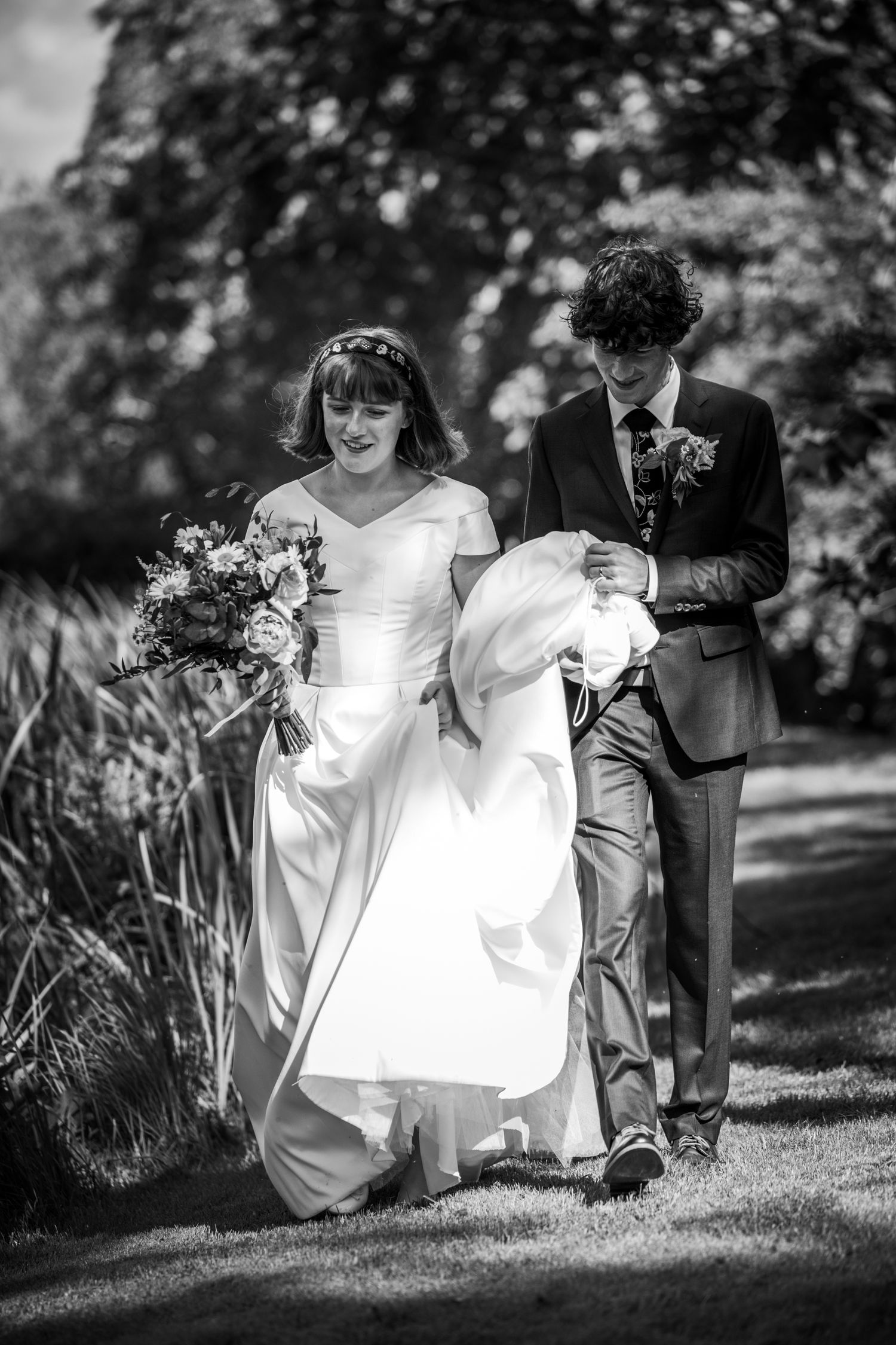 Wedding party members in formal attire walking through a garden setting.