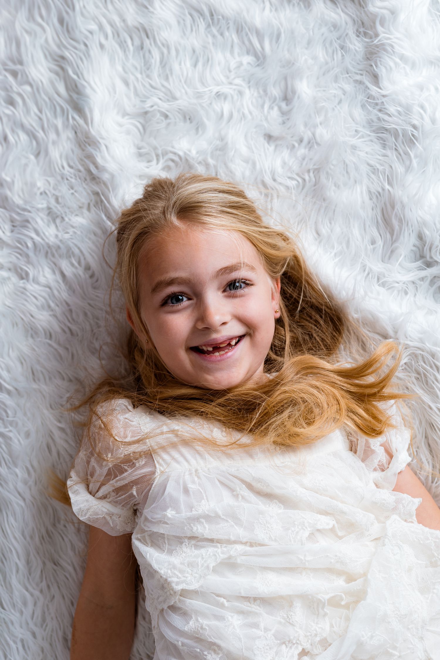 Portrait on white fluffy backdrop showing joyful expression and flowing hair.