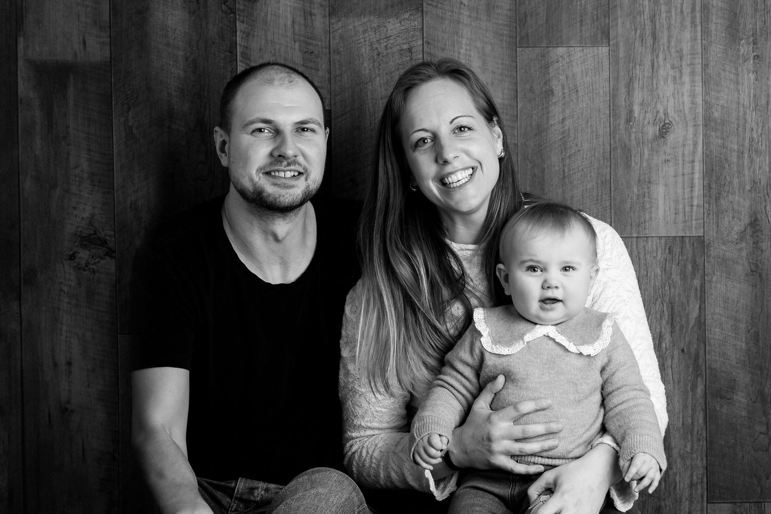 Black and white family portrait against wooden wall background.