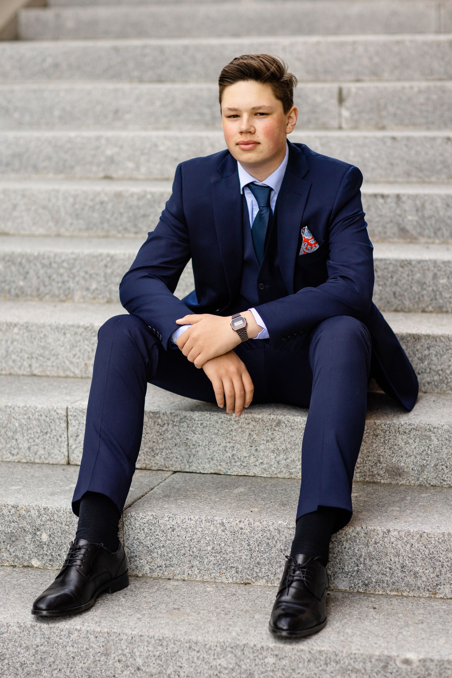 Person in formal navy suit sitting casually on concrete steps outdoors.