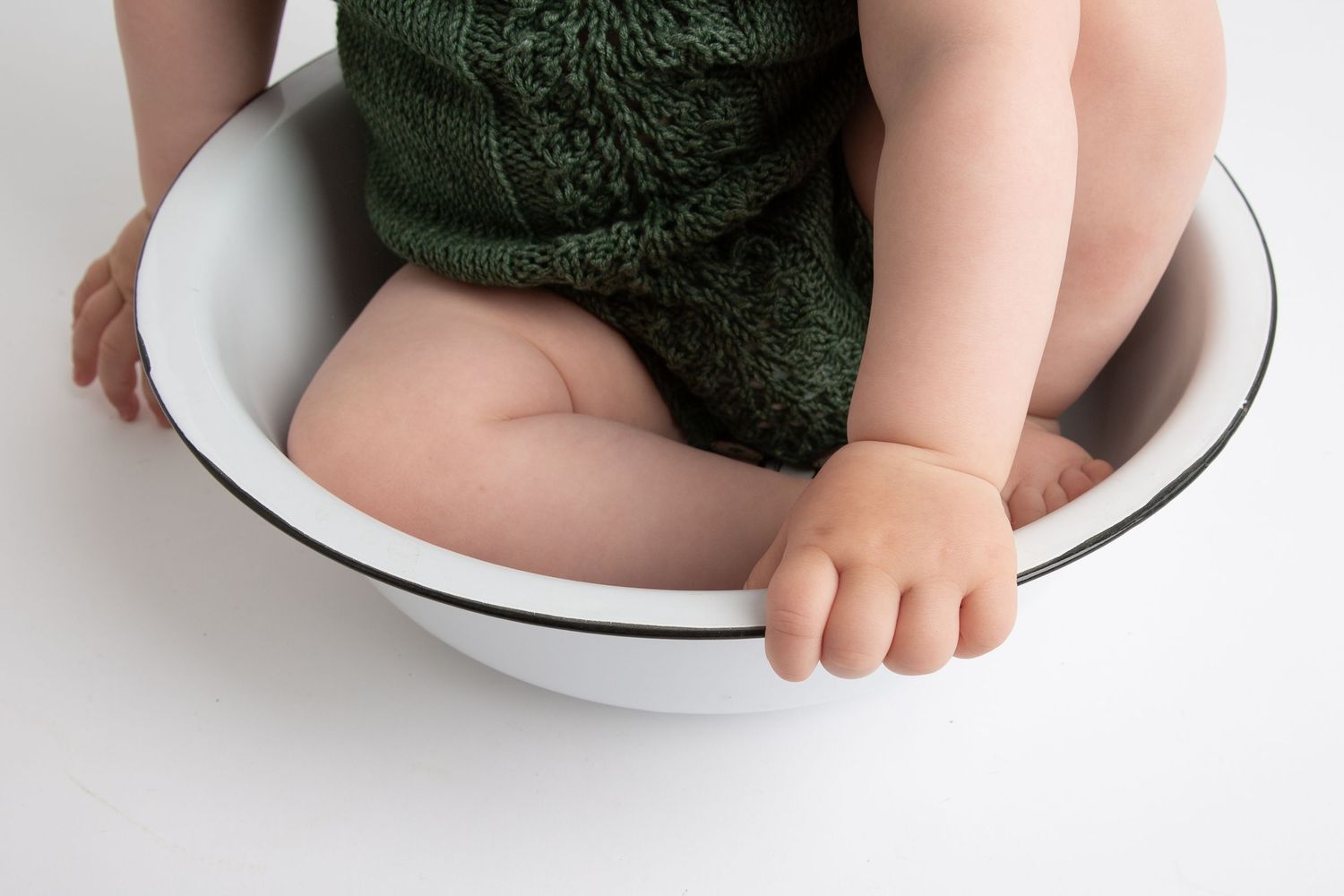 Series of photos showing baby in dark knit outfit sitting in white enamel basin.