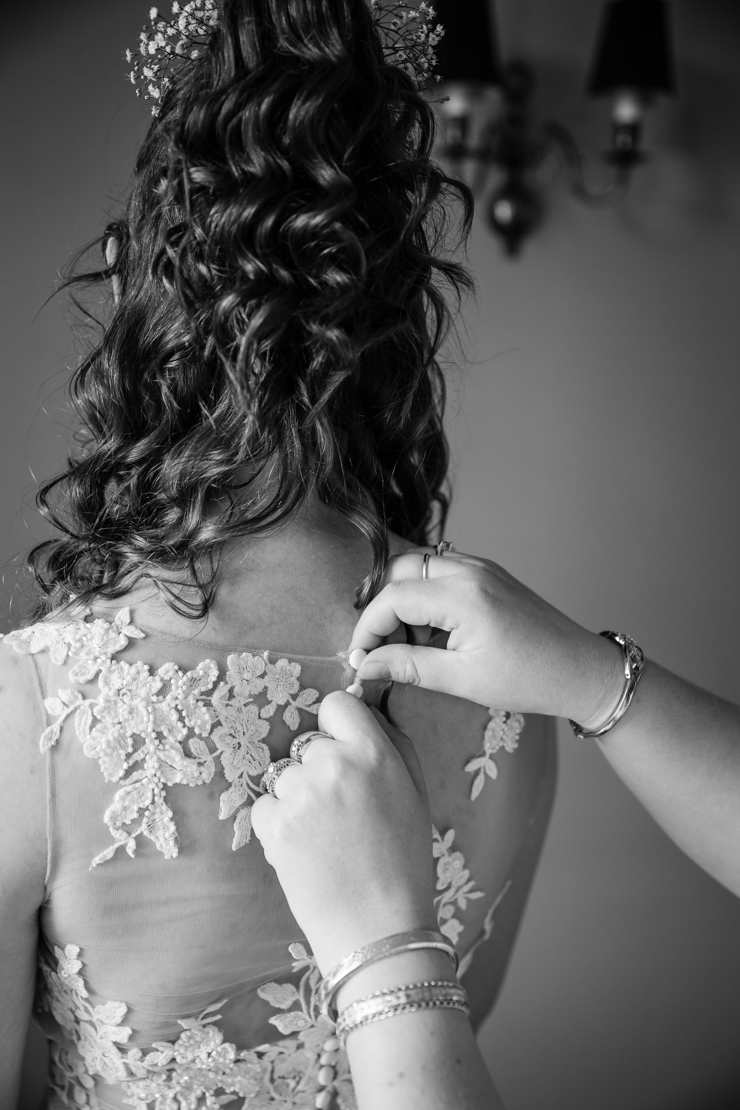 Black and white detail shot of hands buttoning an intricate lace wedding dress.