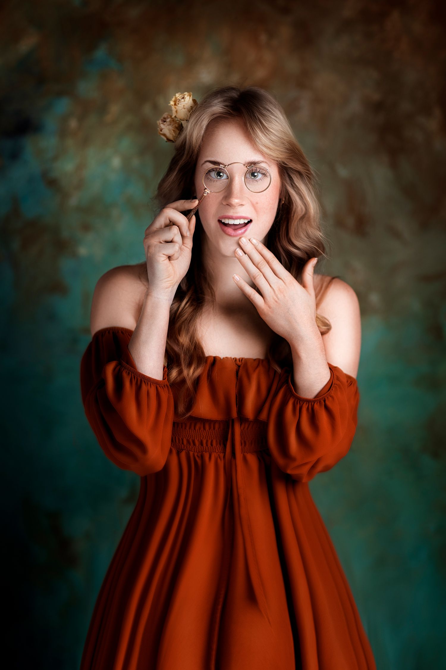 Playful portrait in red off-shoulder dress with glasses against textured teal background.