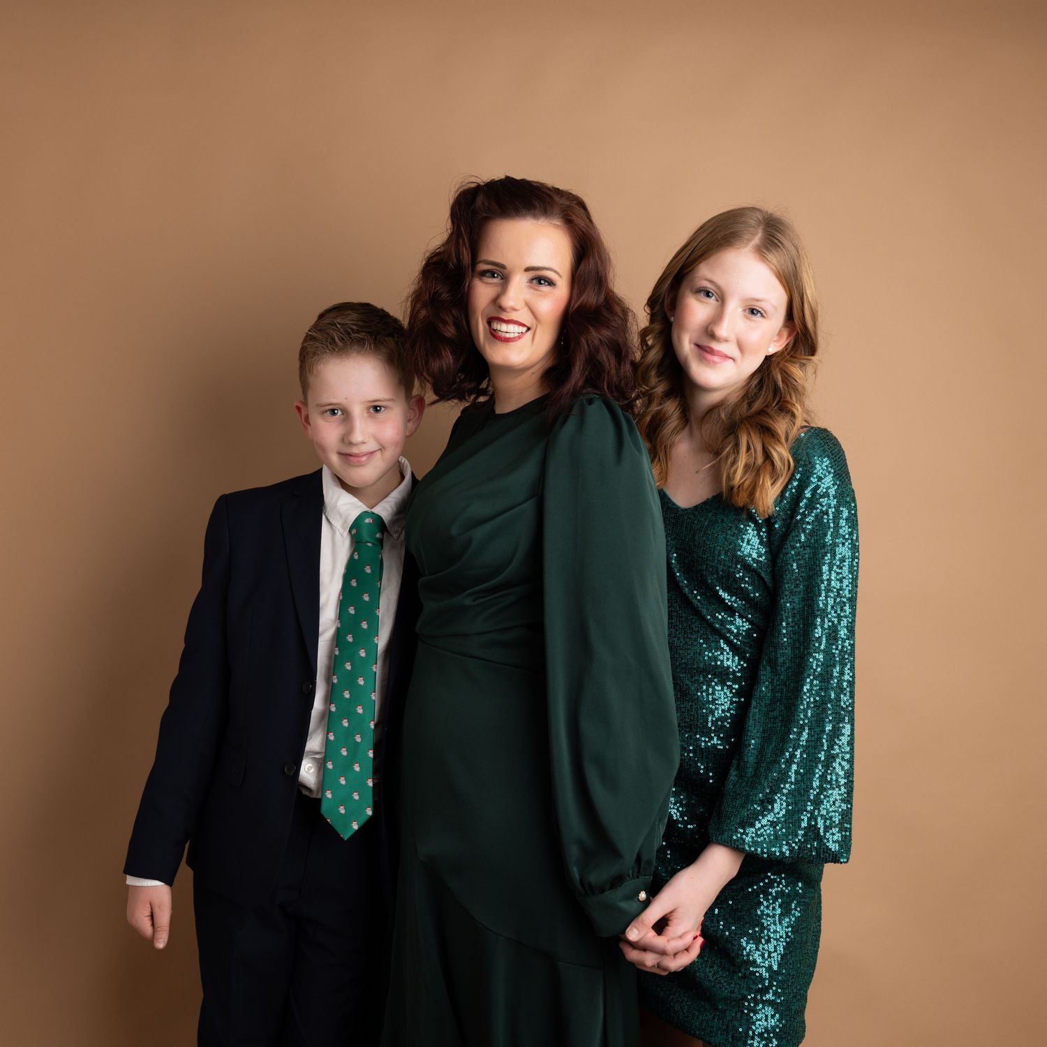 Family in coordinating green and black formal attire posing in studio against beige backdrop.