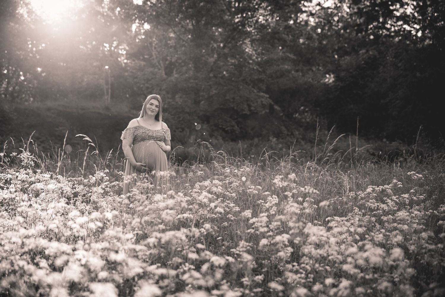 Black and white maternity photos in a field of wildflowers at sunset.