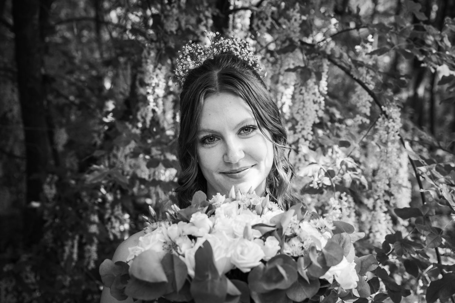Black and white portrait of a bride holding white flowers in a natural outdoor setting.