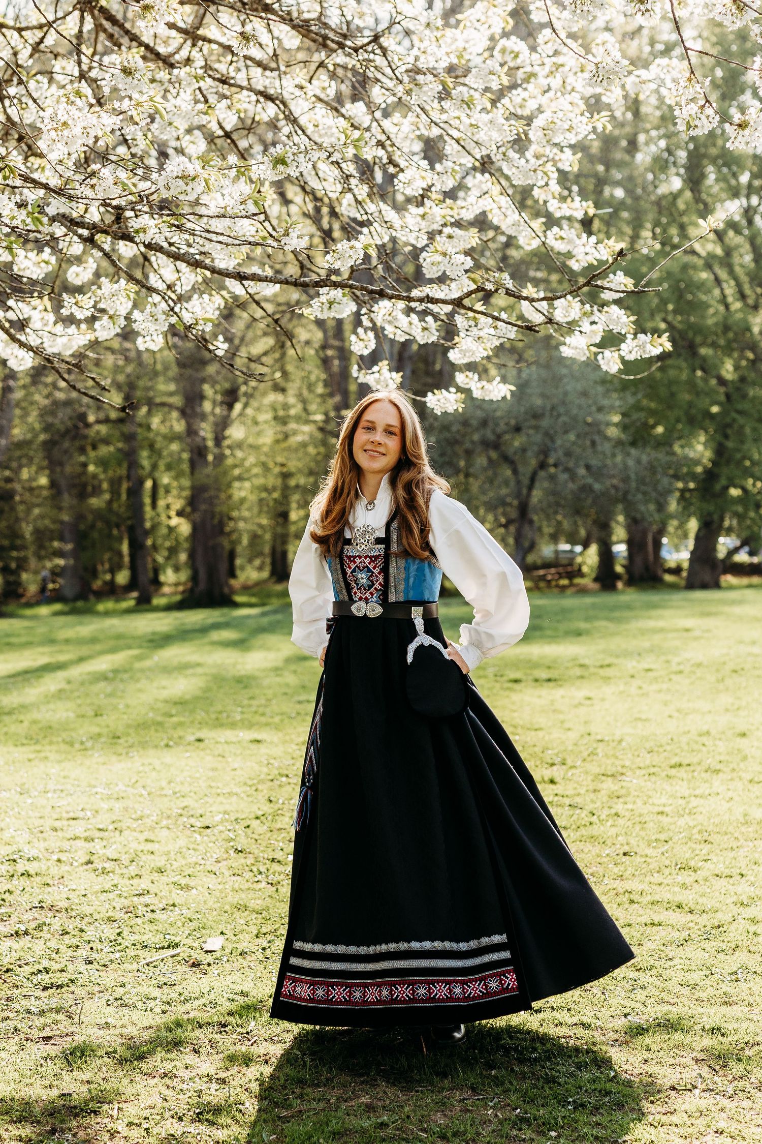 Folk costumes under blooming cherry blossoms in spring garden setting.