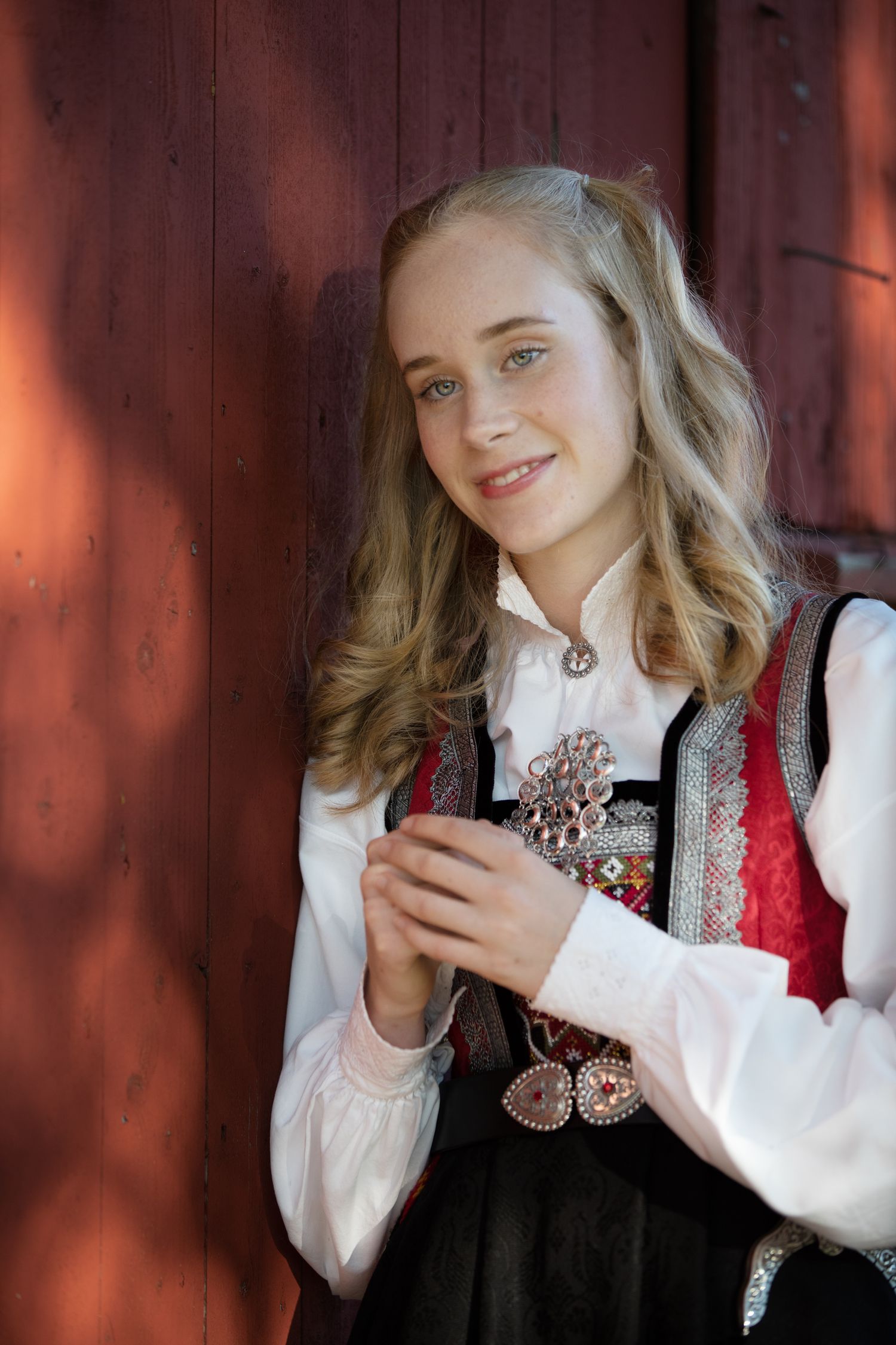 Norwegian bunad costume shown against rustic red barn backdrop.