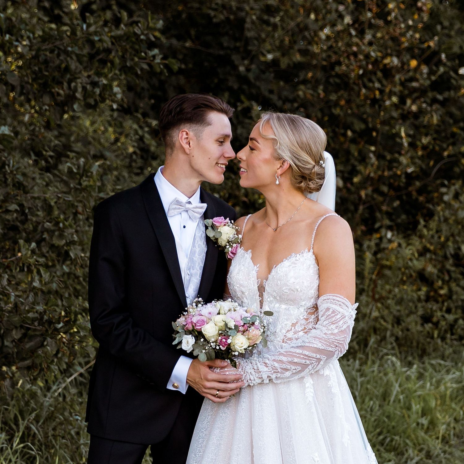 Elegant wedding portrait with bride holding pink bouquet against autumn foliage.