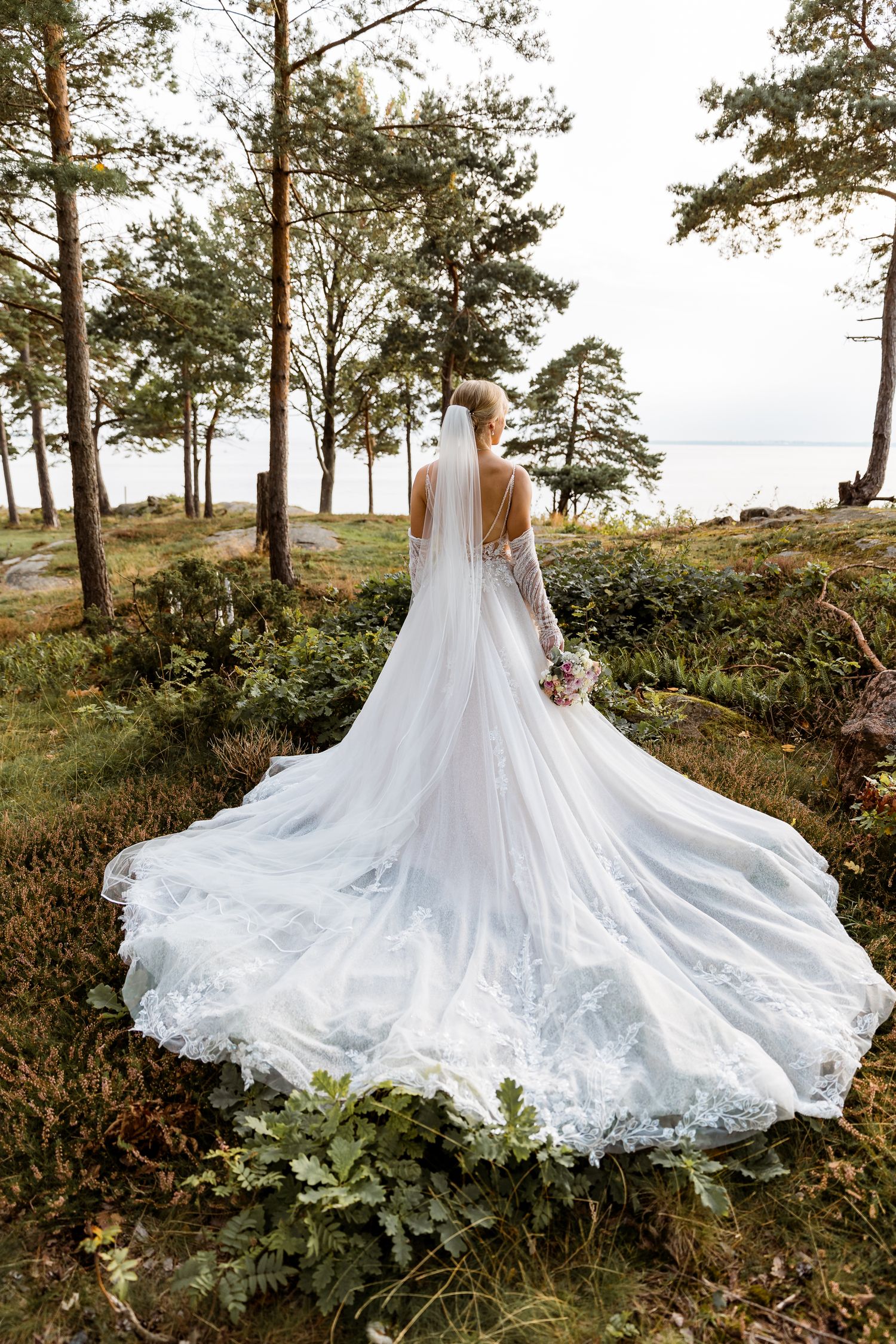 A dramatic wedding dress train spread across forest ground with pine trees in the background.