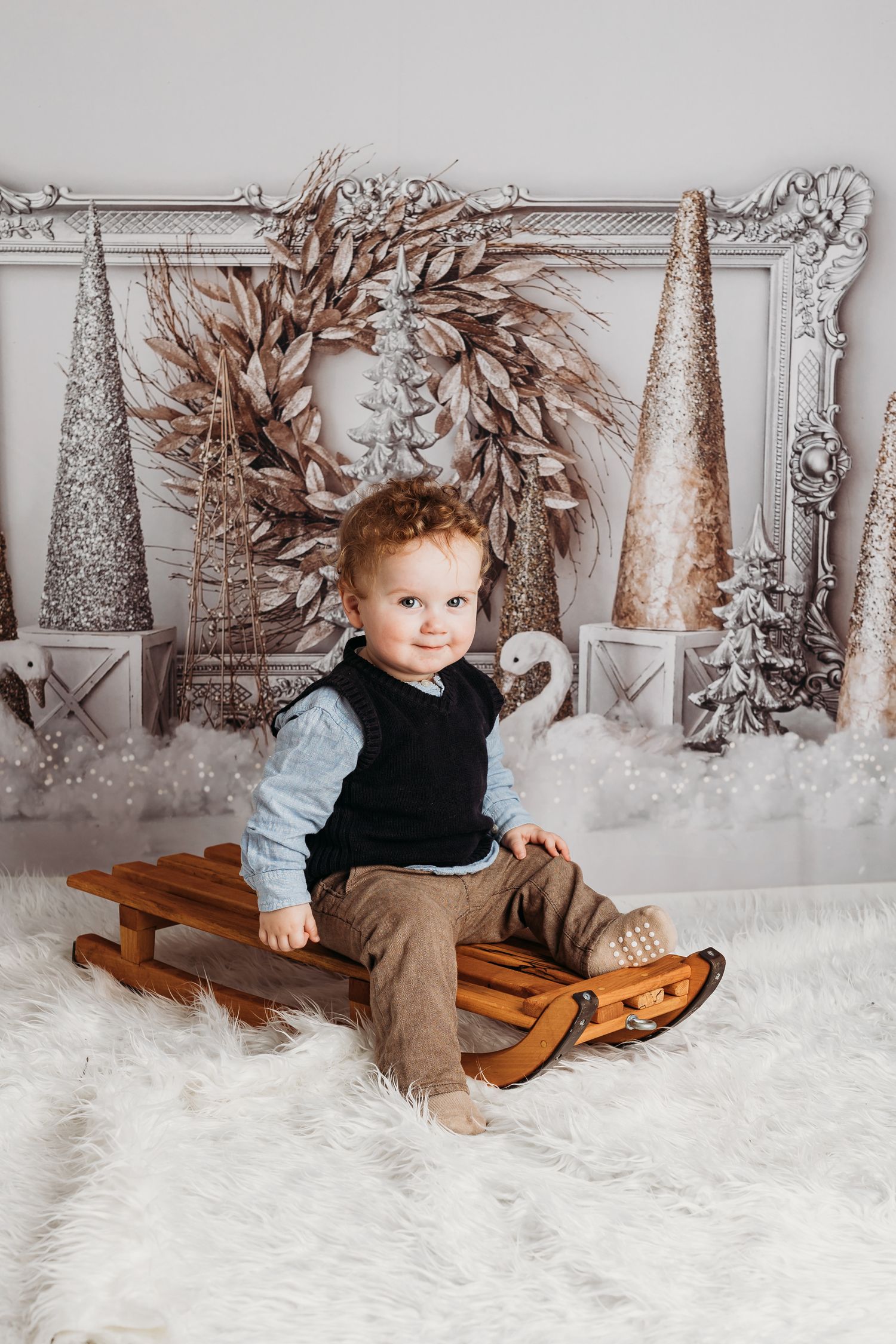 Cozy winter photo setup with wooden sled and silver decorative trees on white furry rug.