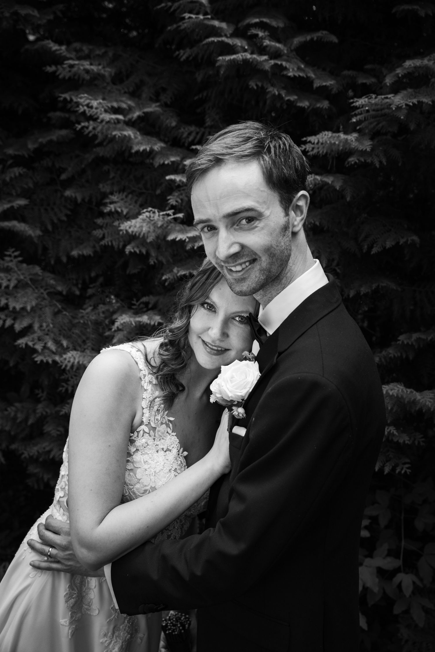 Black and white portrait of wedding couple sharing intimate moment against evergreen trees.