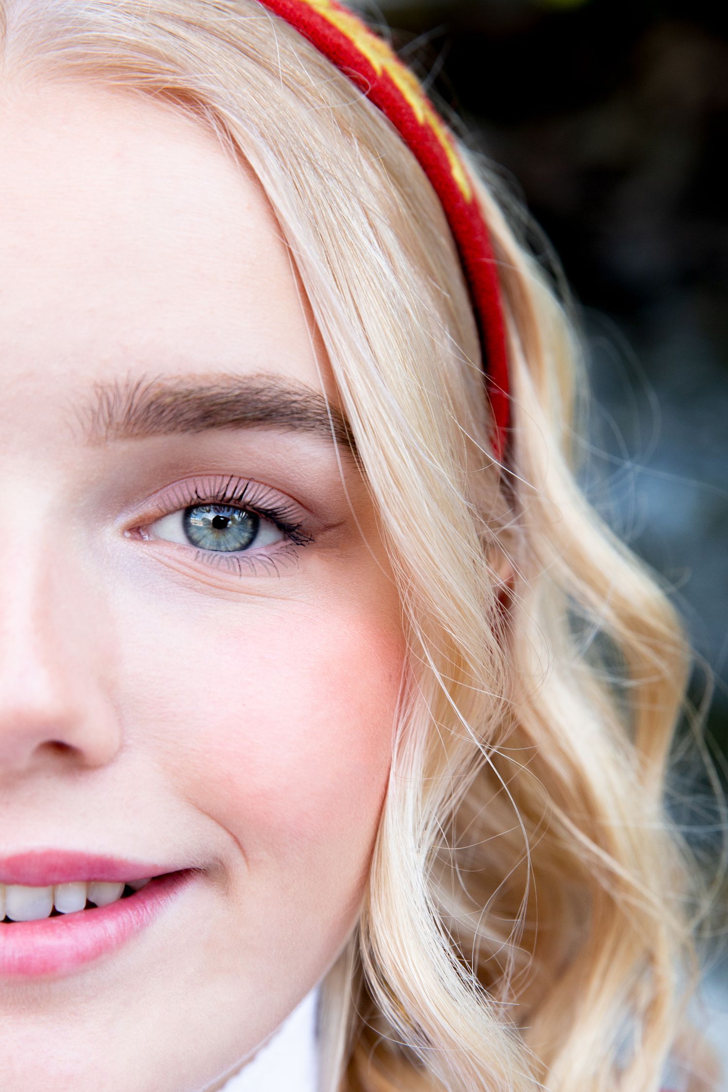 A close-up beauty portrait showing bright eyes, red headband and blonde wavy hair.