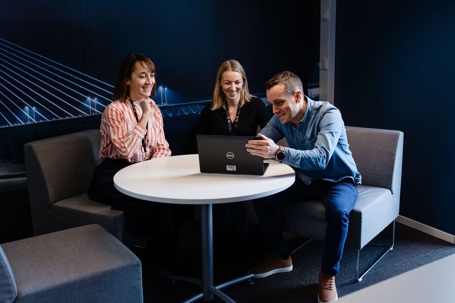 People gathered around white table in modern office meeting space with dark lighting.