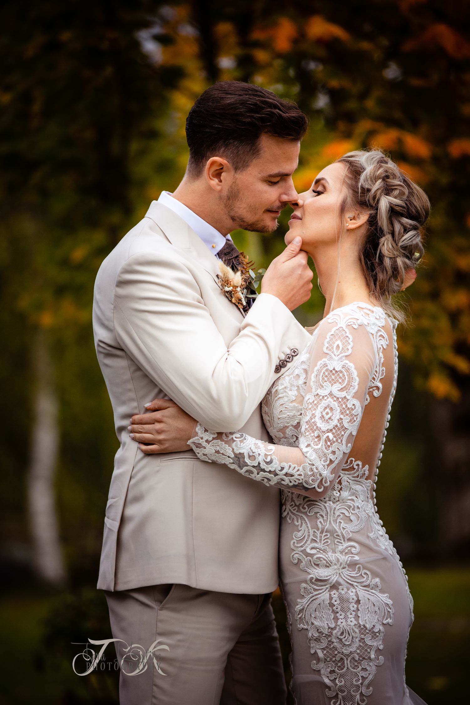 Wedding couple sharing romantic moments in autumn forest wearing elegant white dress and beige suit.