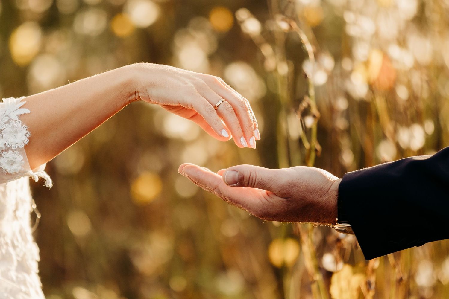 Close-up of hands exchanging rings during wedding ceremony with golden bokeh background.