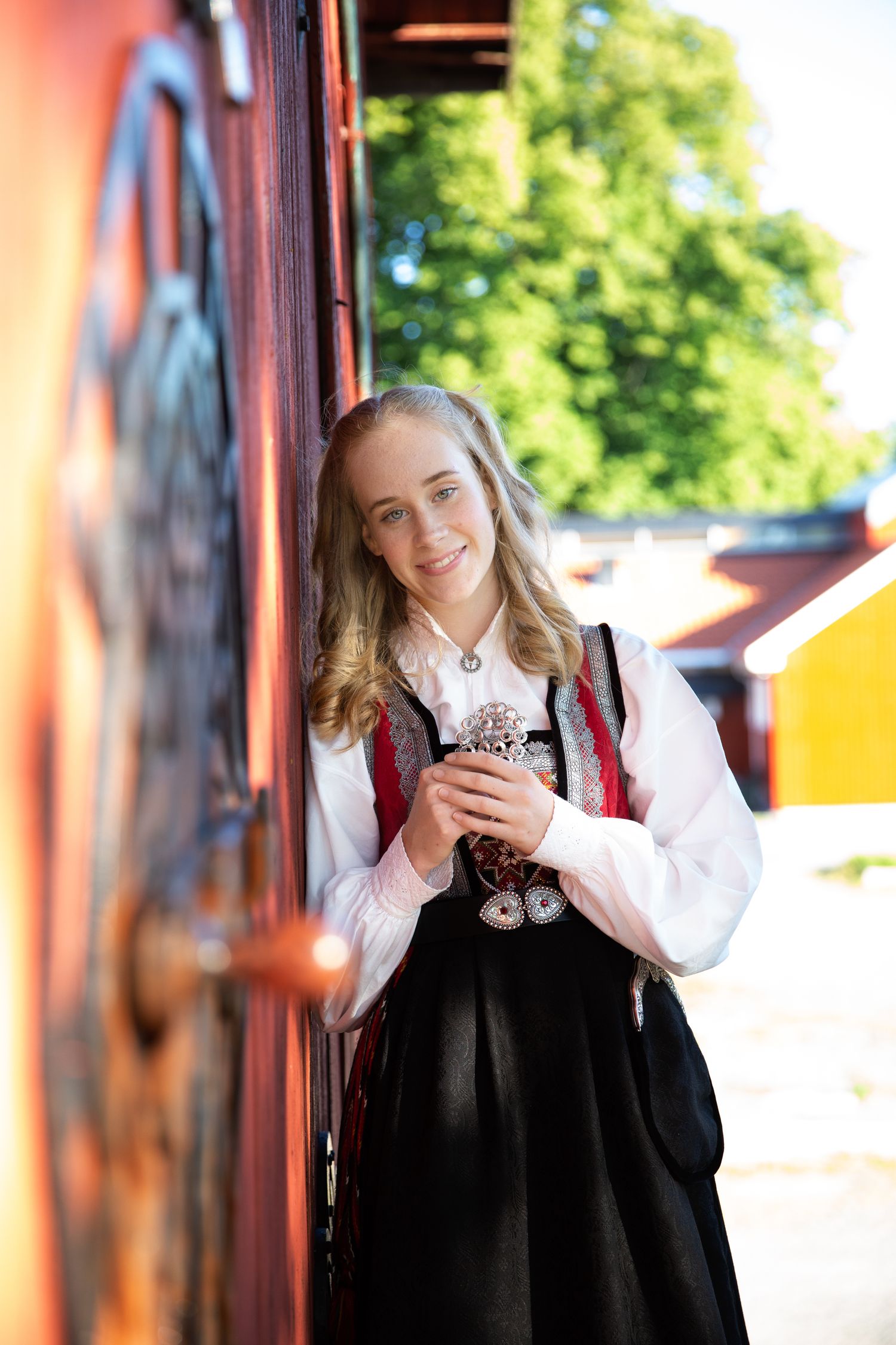 A person in traditional dress with white blouse and black pinafore poses against a colorful wall outdoors.