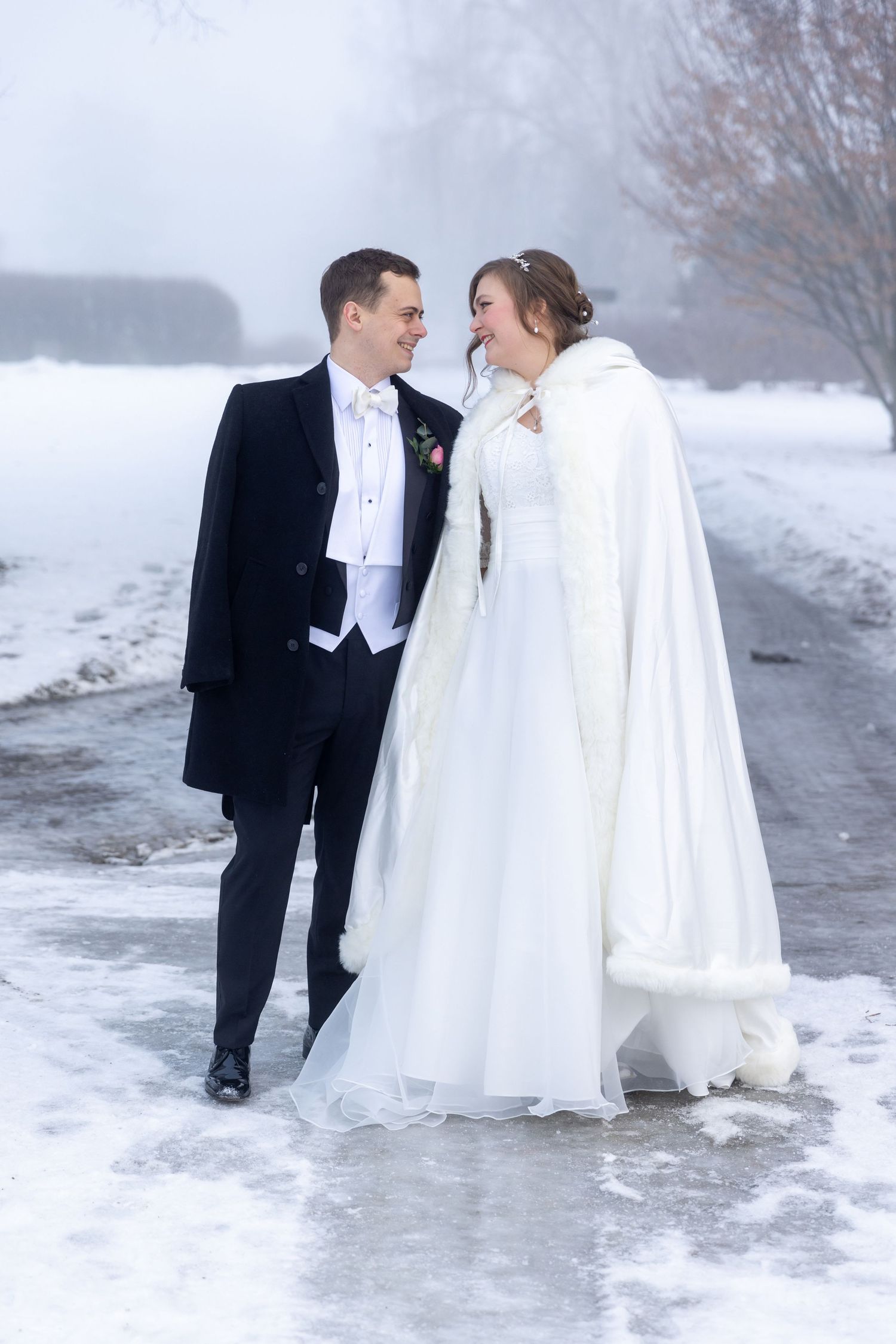 Wedding couple poses against stone archway with bride in lace gown and groom in classic tuxedo.