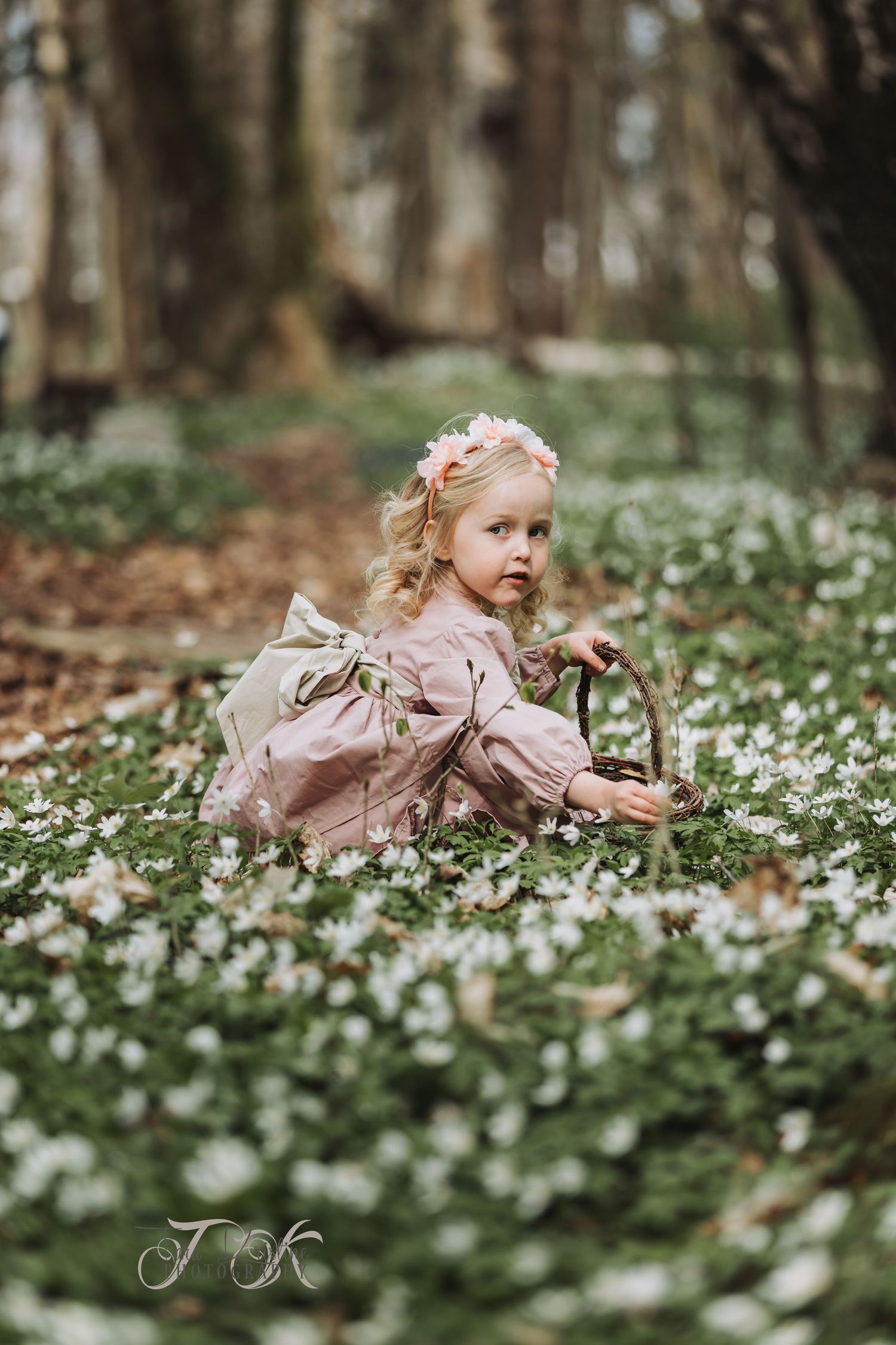 Dreamy portrait of small figure among blooming woodland flowers in soft lighting.