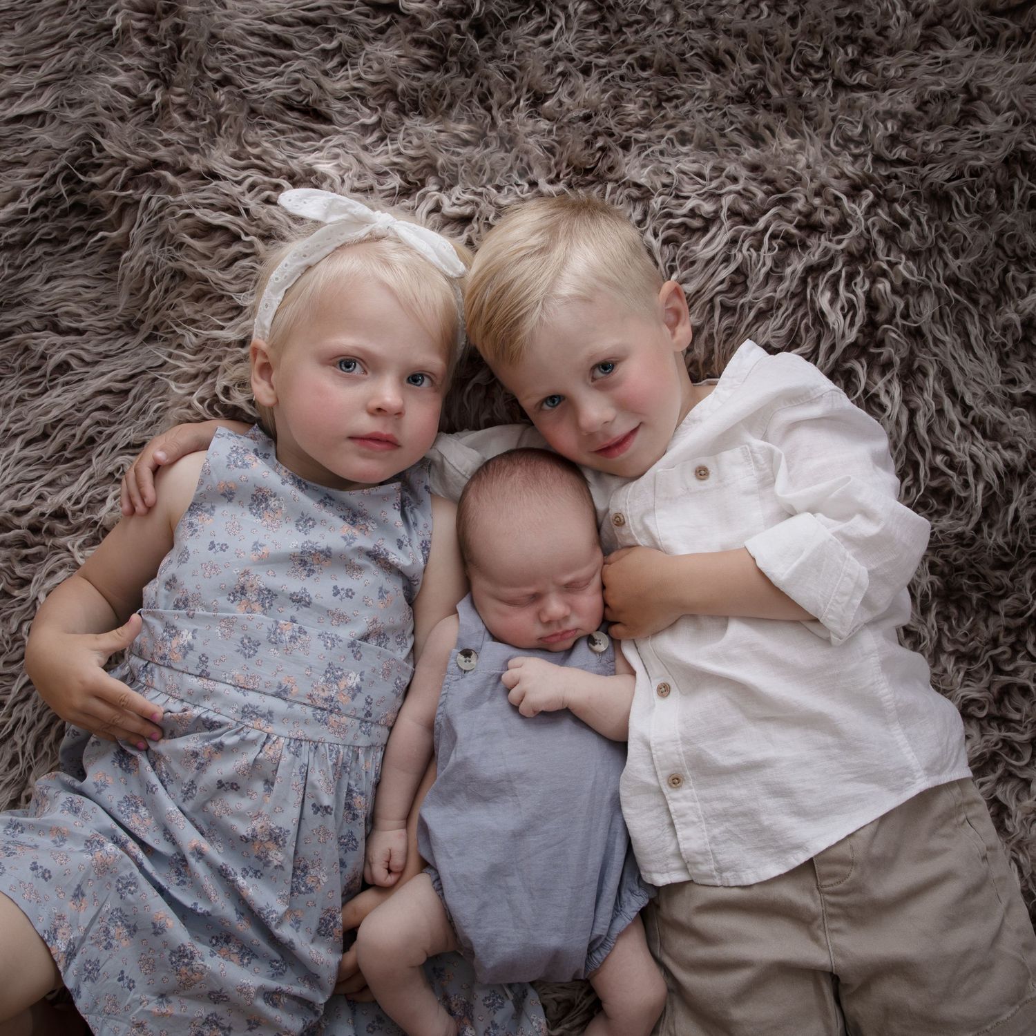 Children lying together on soft gray carpet during intimate portrait session.