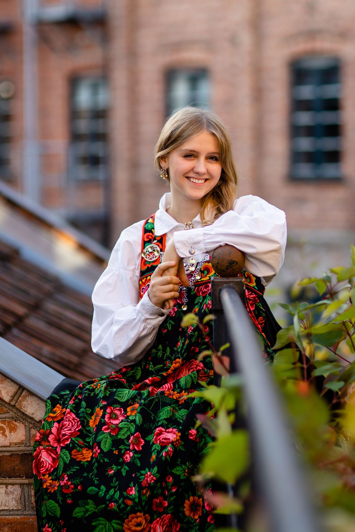 Folk costume featuring white blouse and floral embroidered vest against brick building backdrop.