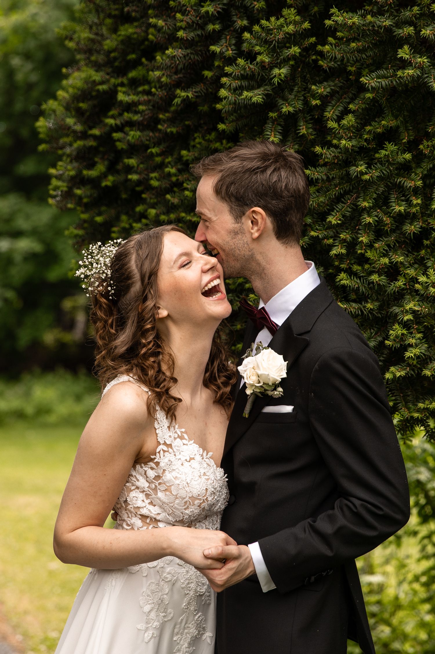 Candid moment of newlyweds laughing together against green garden backdrop.