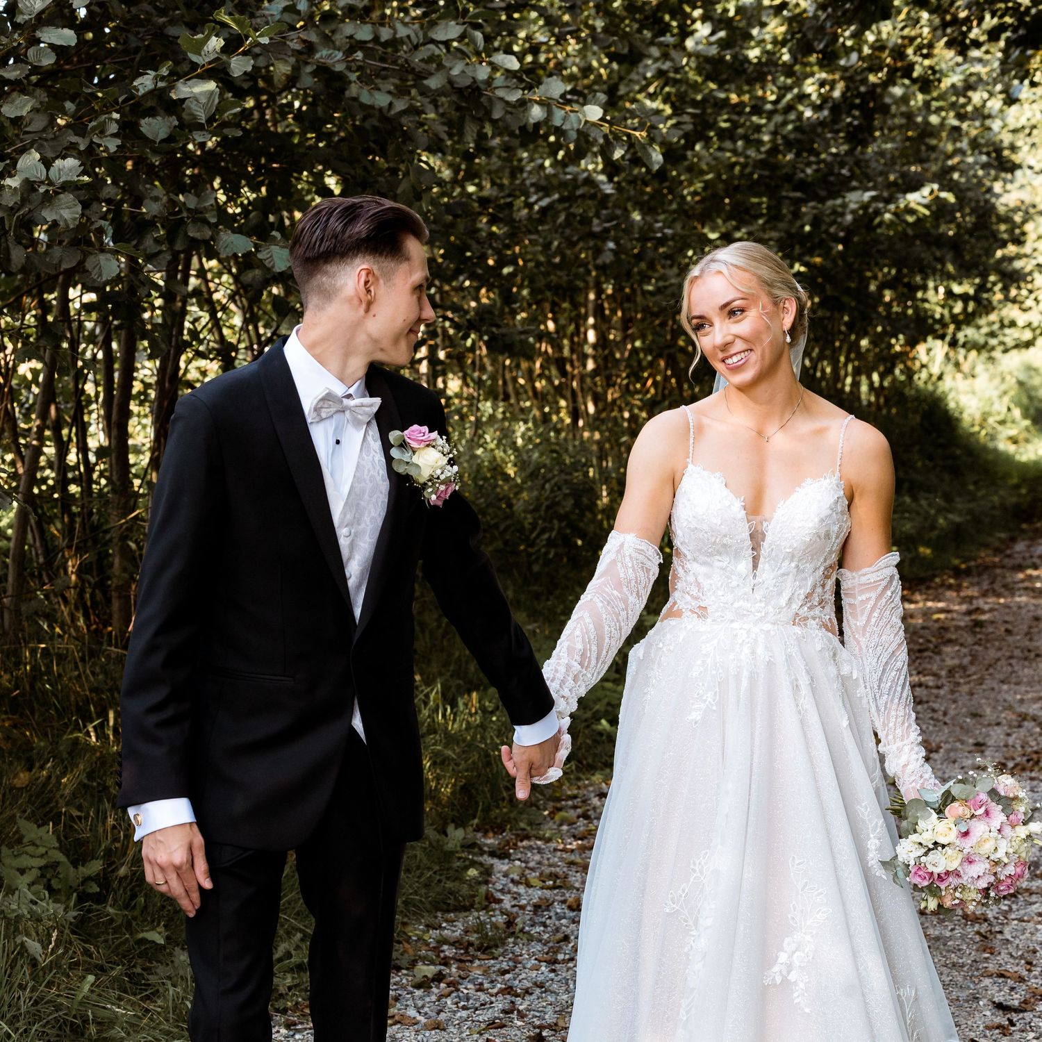 Wedding couple walking together through a wooded path in formal attire.
