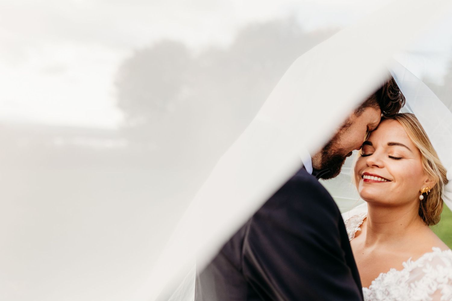 Romantic couple embracing under a white veil during their wedding photoshoot.