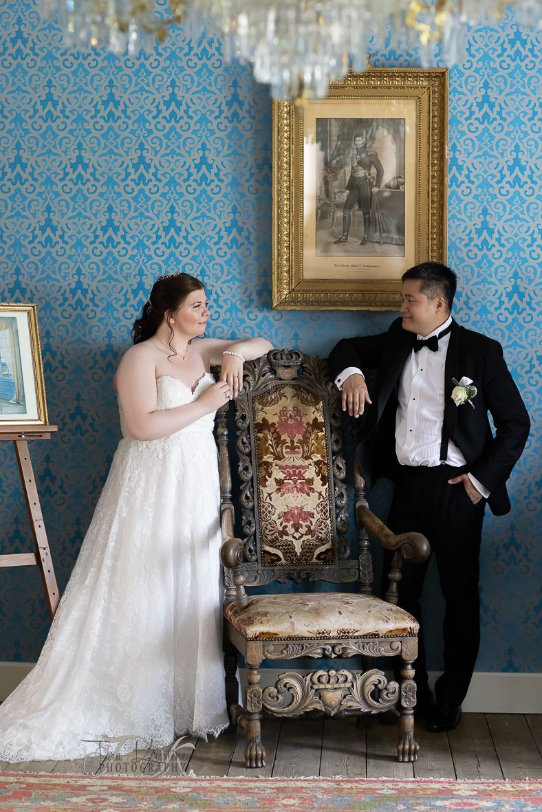 A couple poses playfully in an elegant blue-wallpapered room with ornate furniture.