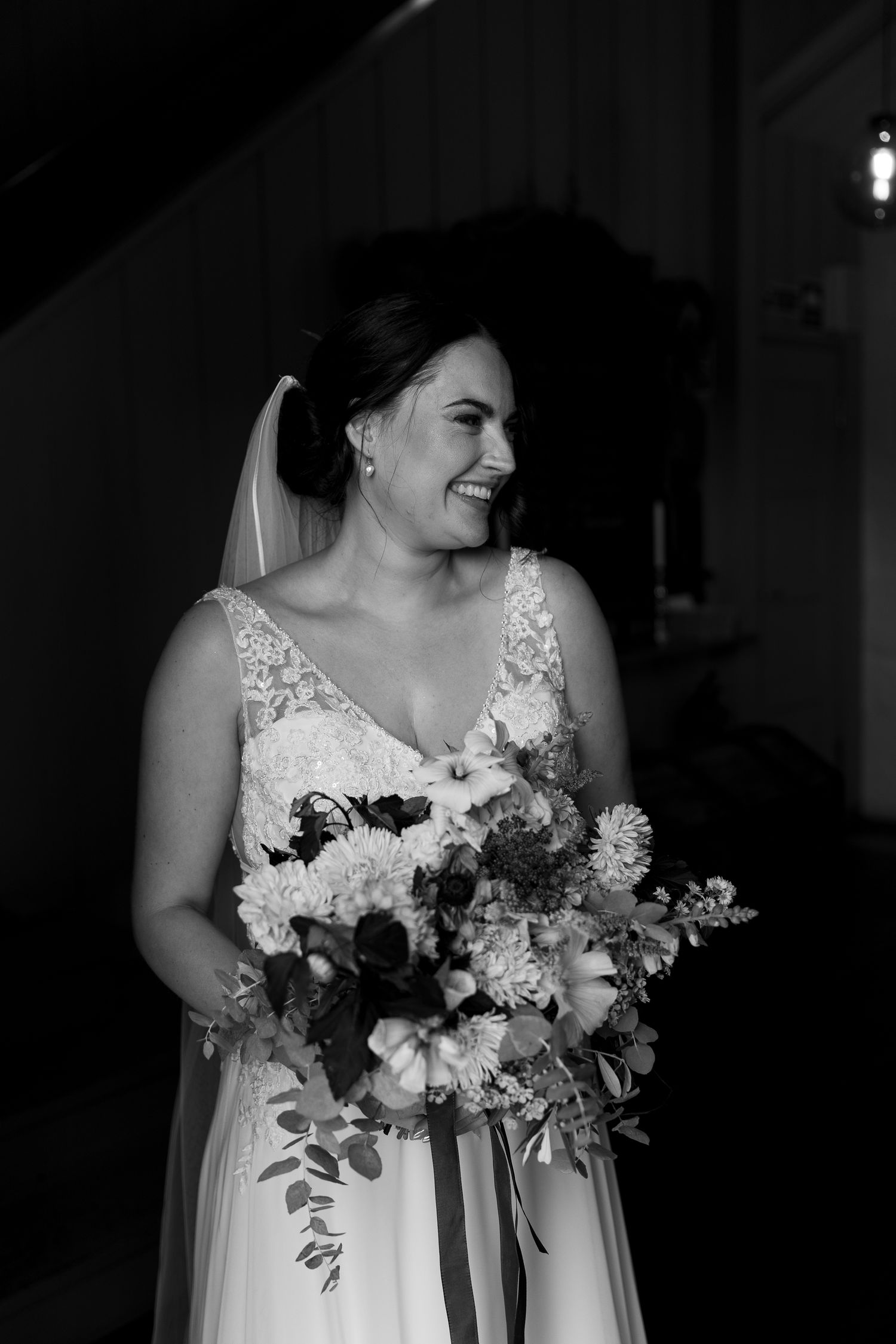 Black and white portrait of a joyful bride holding a lush bouquet of mixed flowers.