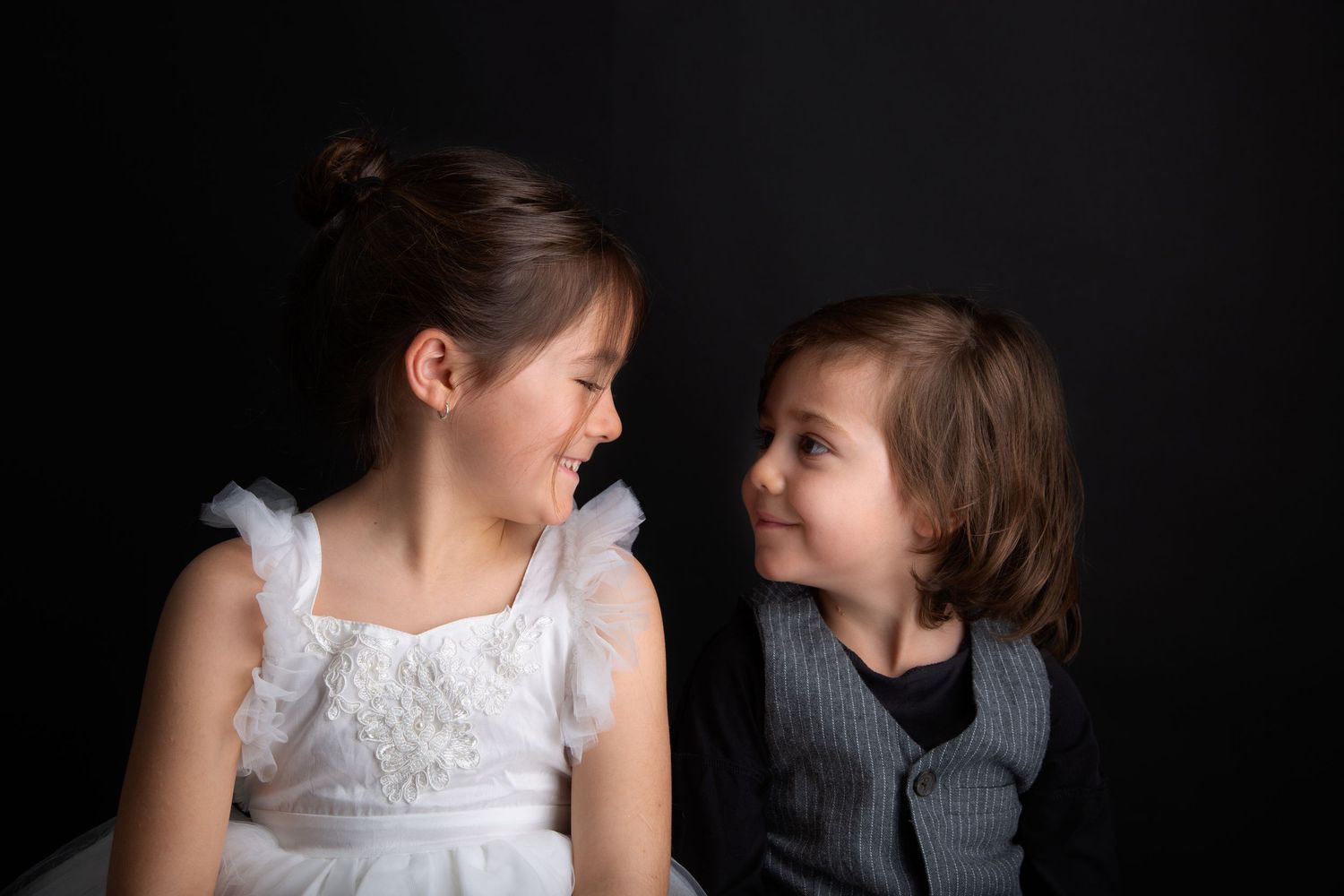 Artistic black and white portrait of siblings in contrasting outfits against dark background.