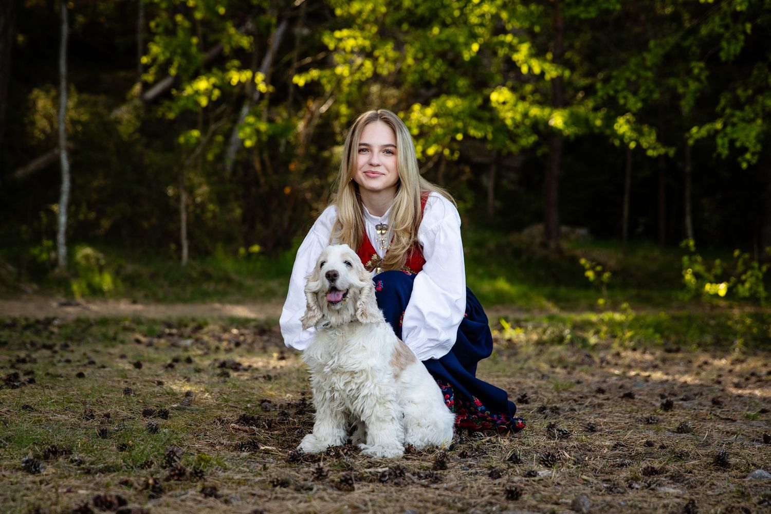 White fluffy dog poses with someone wearing traditional Norwegian clothing outdoors in autumn.