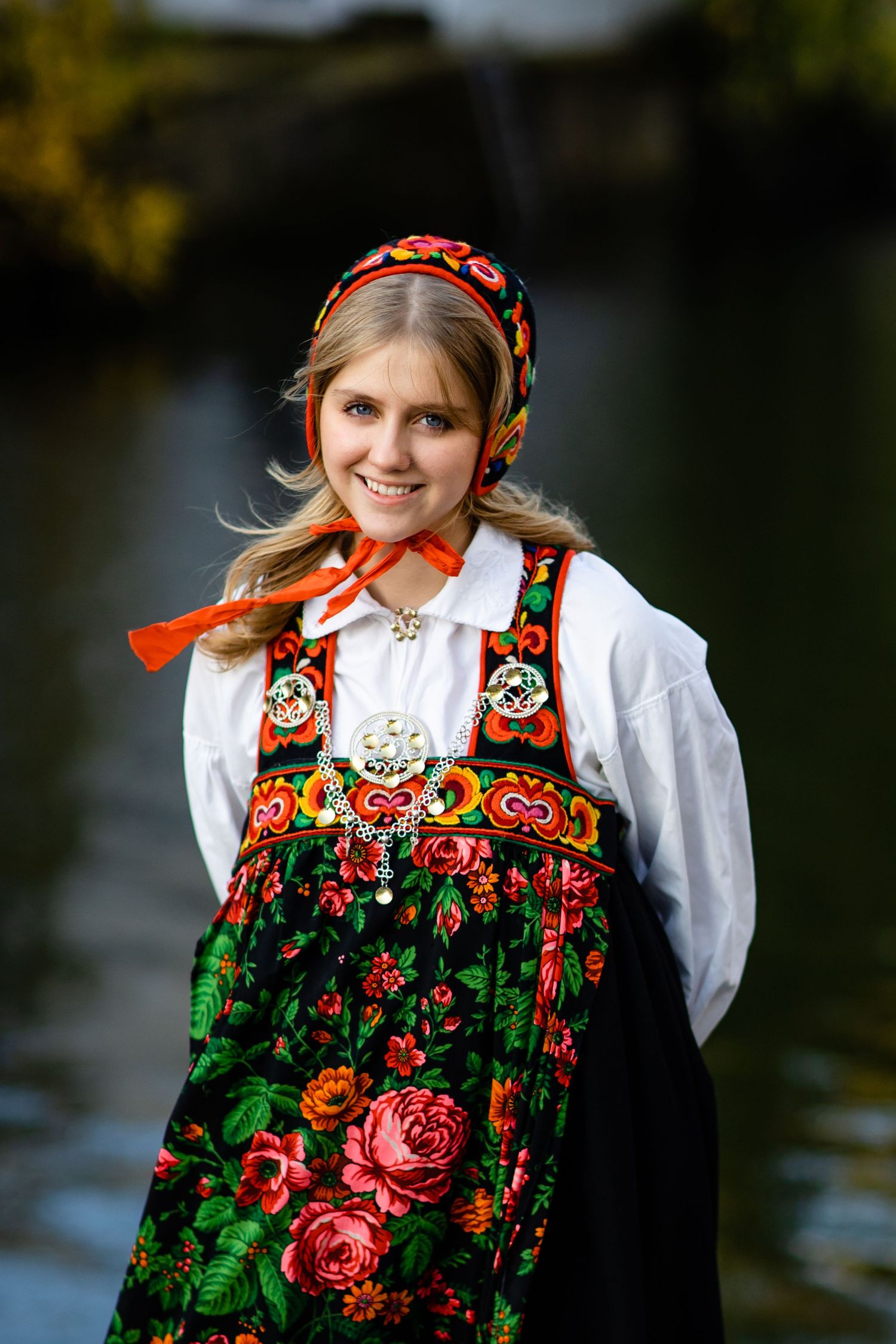 Traditional folk costume with red headscarf and floral embroidered vest photographed by water.