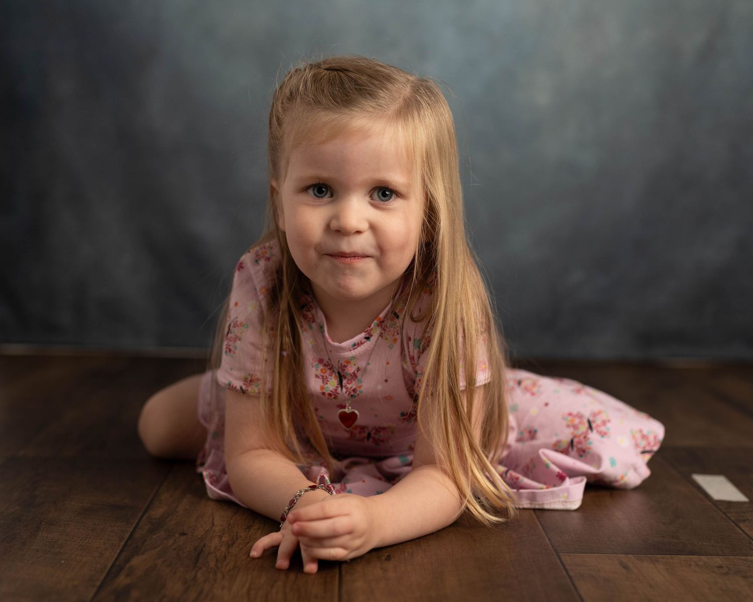 Studio portrait on wooden floor with pink dress and natural lighting.