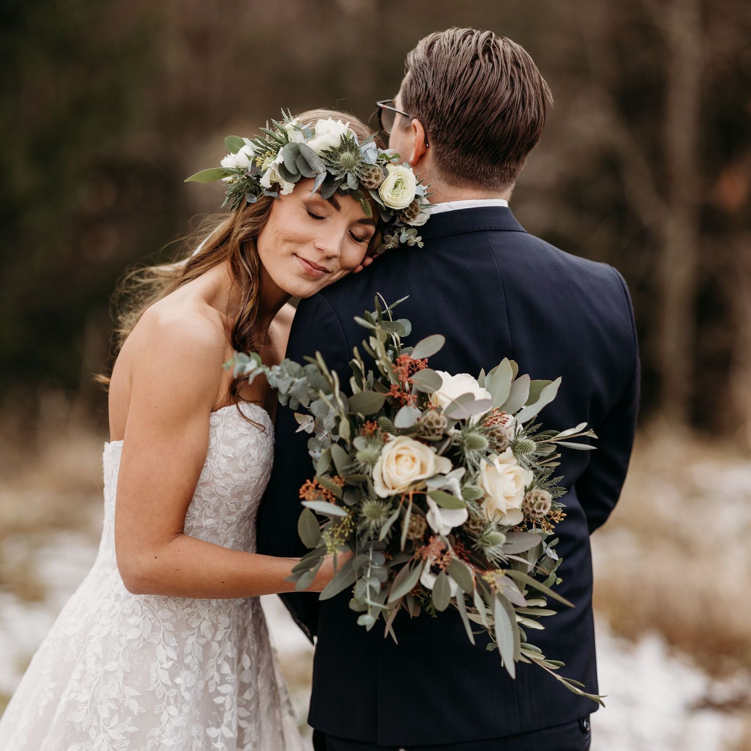 Wedding couple embraces among greenery with elegant white floral bouquet.