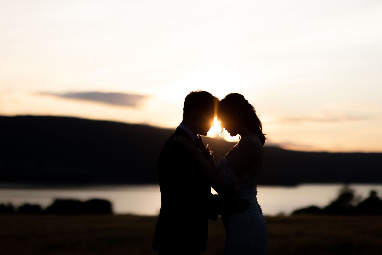 Silhouetted couple shares romantic moment against sunset sky over water.