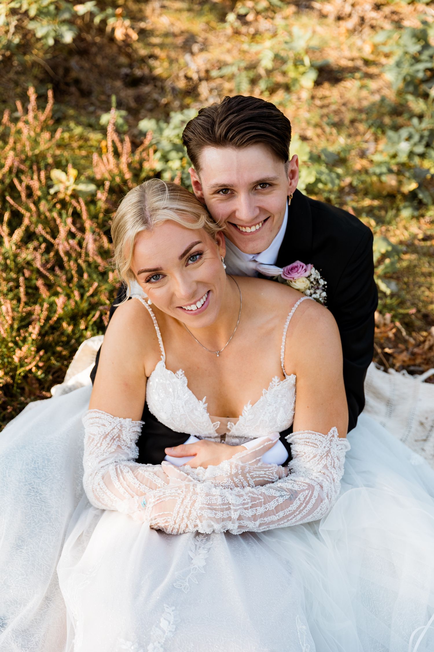 A romantic wedding portrait showing a couple in formal attire laying in autumn foliage.