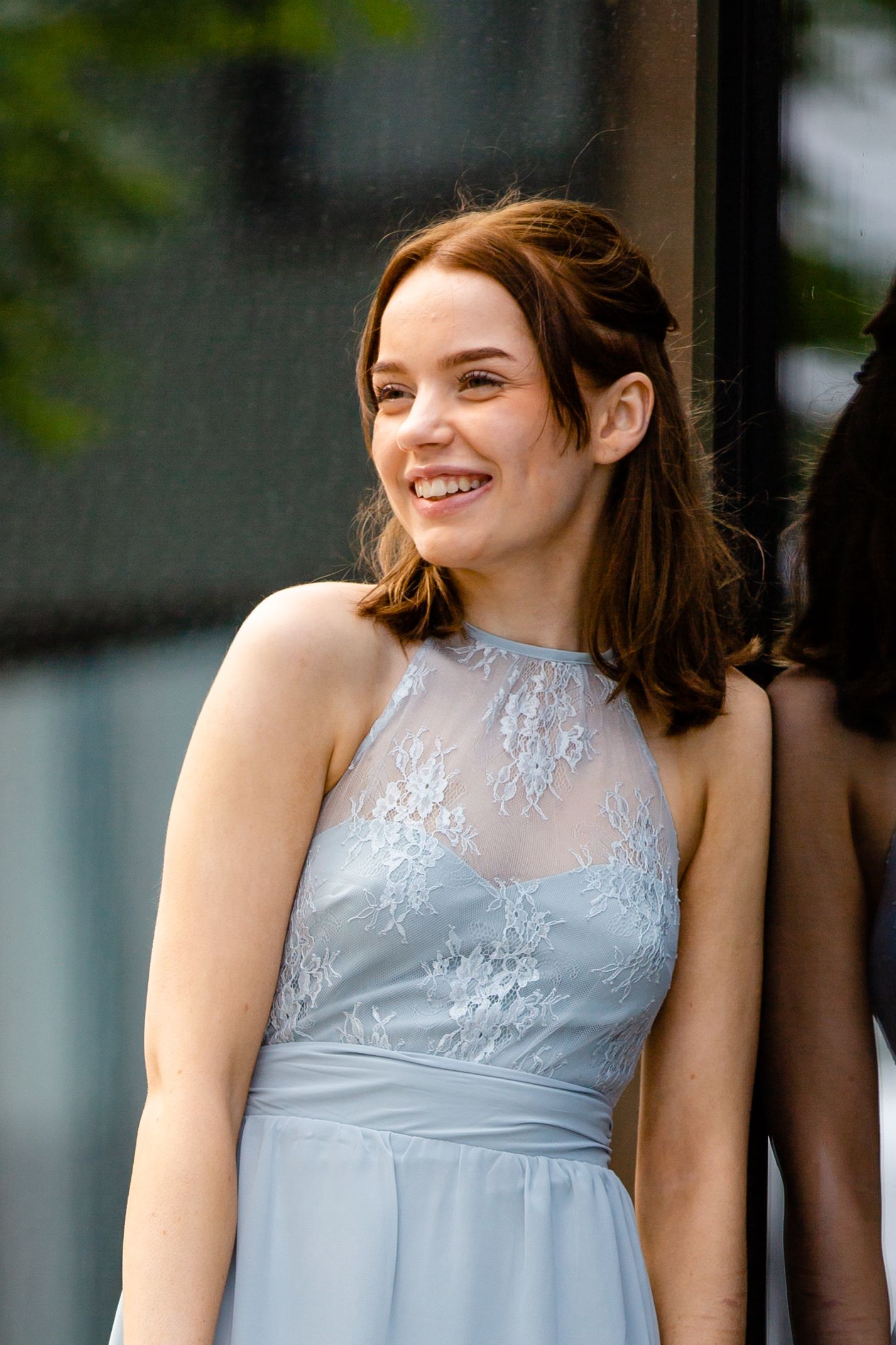 A person in a light blue formal dress with lace detailing smiles warmly while looking to the side.