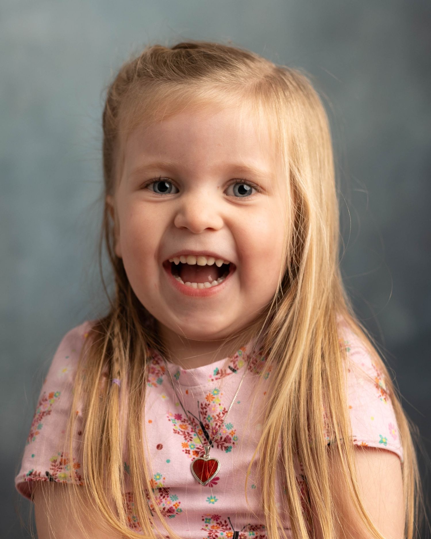 Joyful studio portrait with pink floral top against blue-grey background.