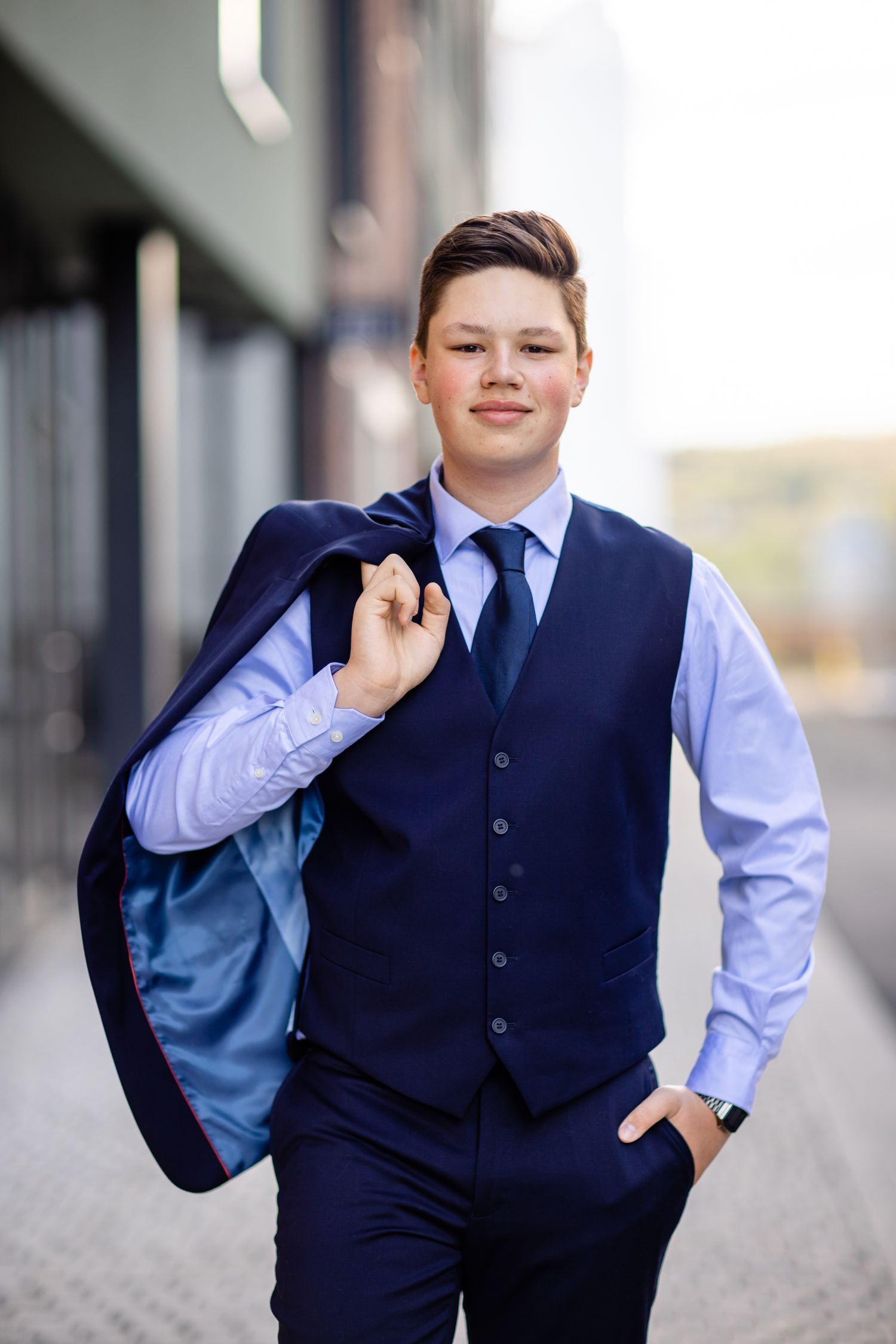 Young person in navy suit and light blue dress shirt poses confidently in an urban setting.