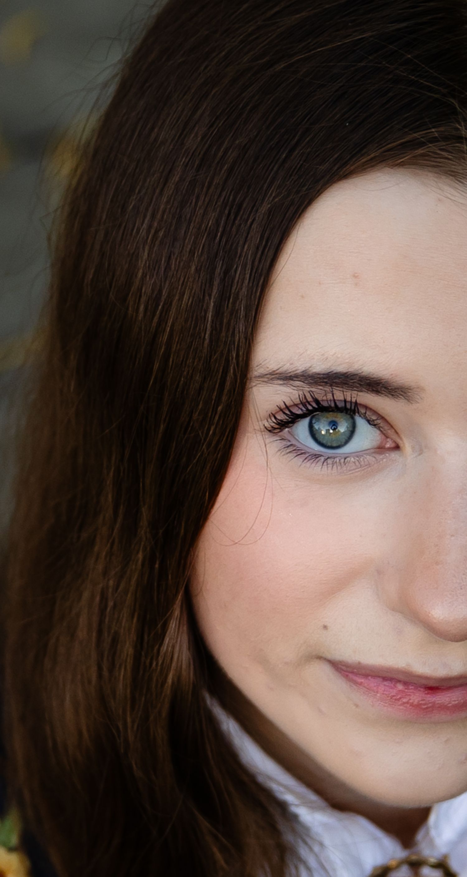 Close up portrait showing bright blue eye and subtle smile against natural background.