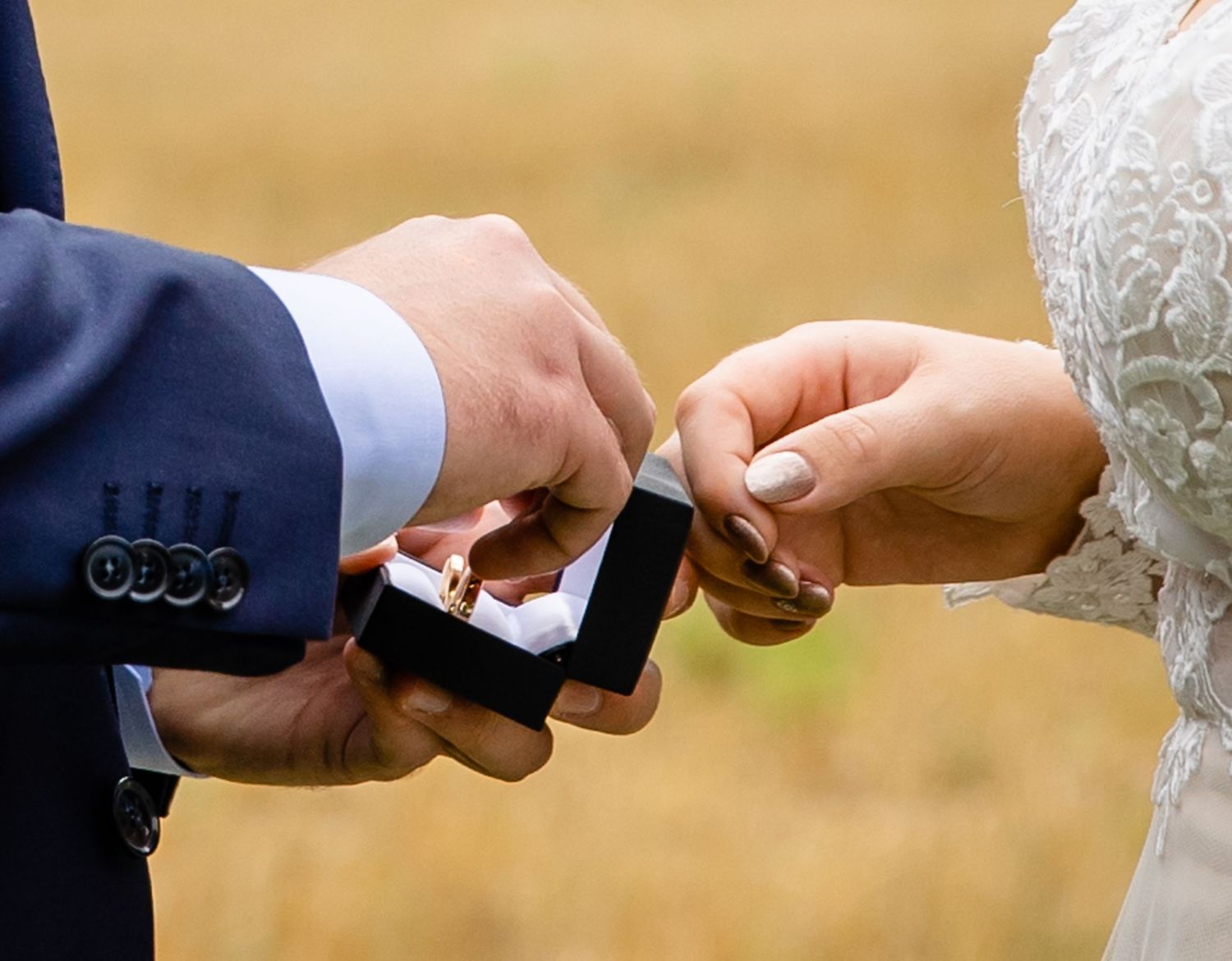 Close-up of wedding couple exchanging rings during outdoor ceremony.