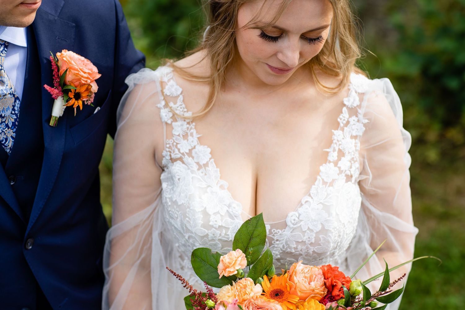 Wedding couple in navy suit and lace dress with orange bouquet.