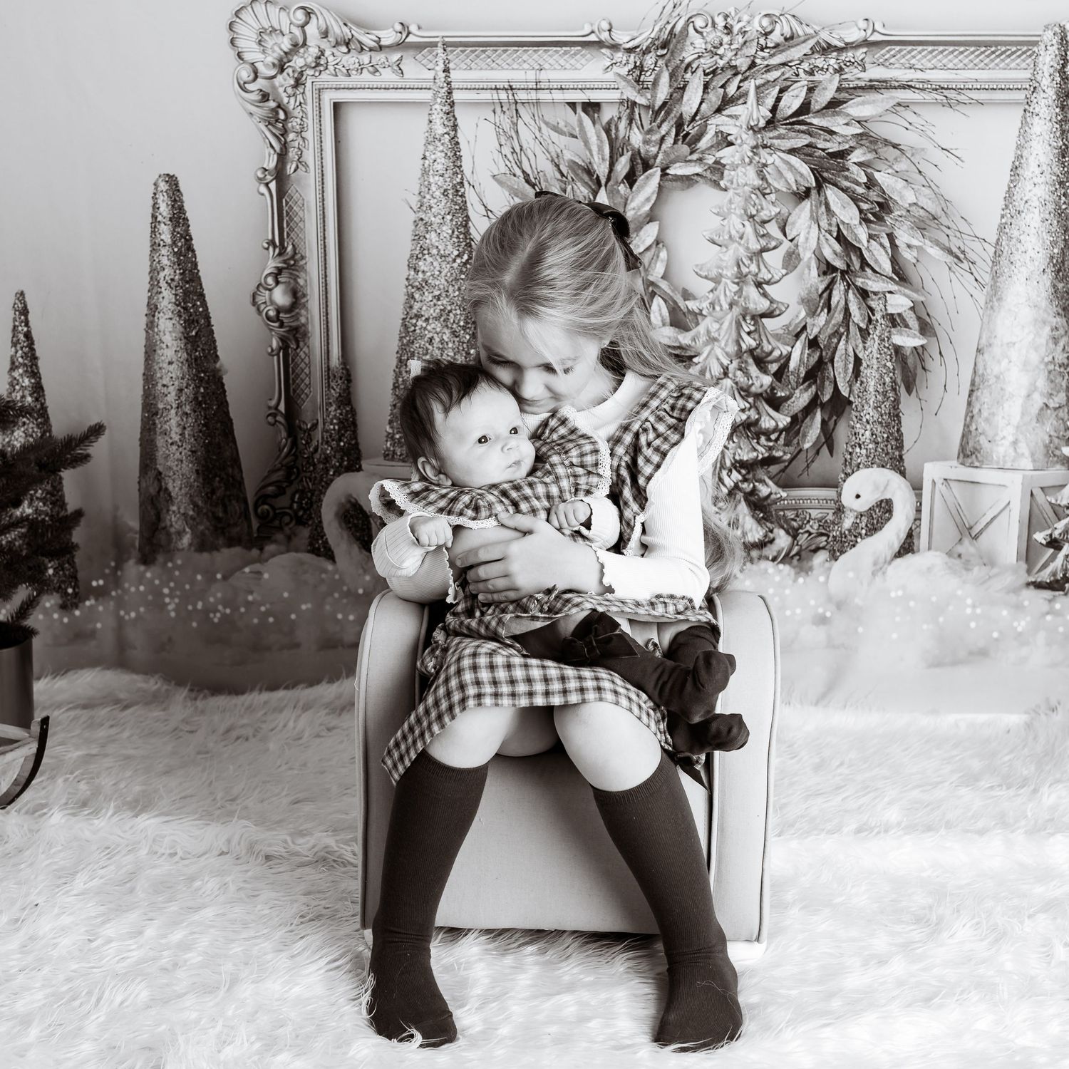 Child in checkered dress sitting on floor with stuffed animals in winter themed studio backdrop.