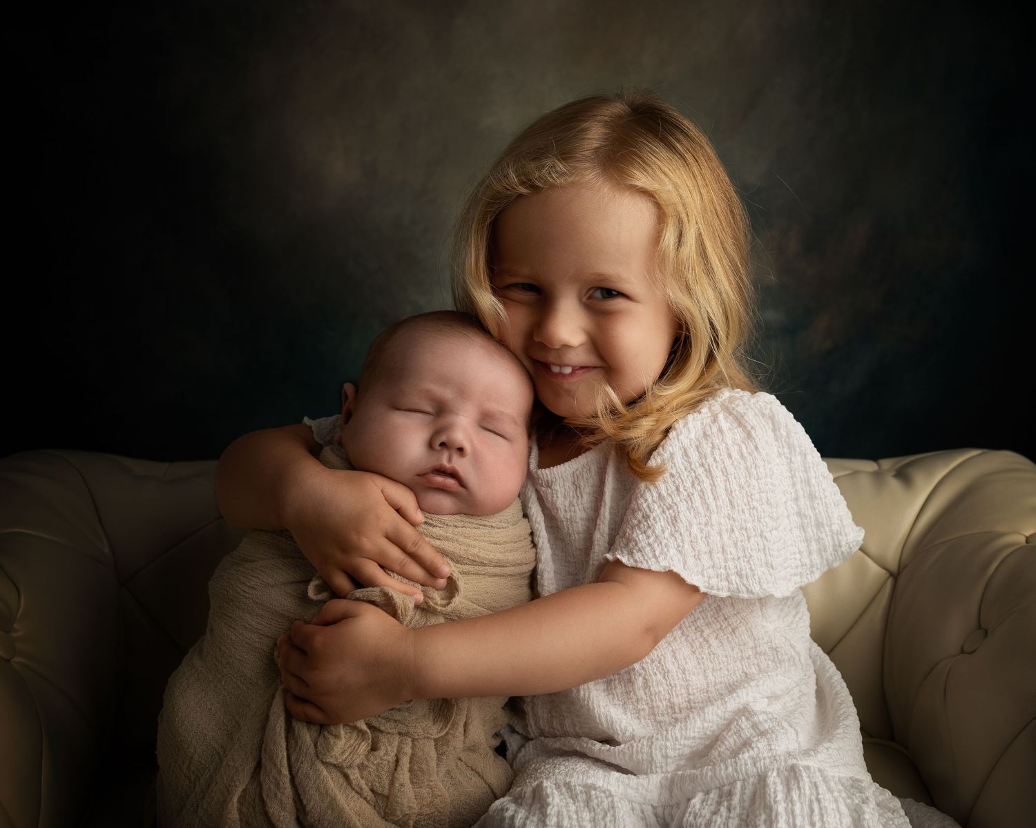 Storesøster holder nyfødt baby tett inntil seg under søskenfotografering i studio hos fotograf i Moss.