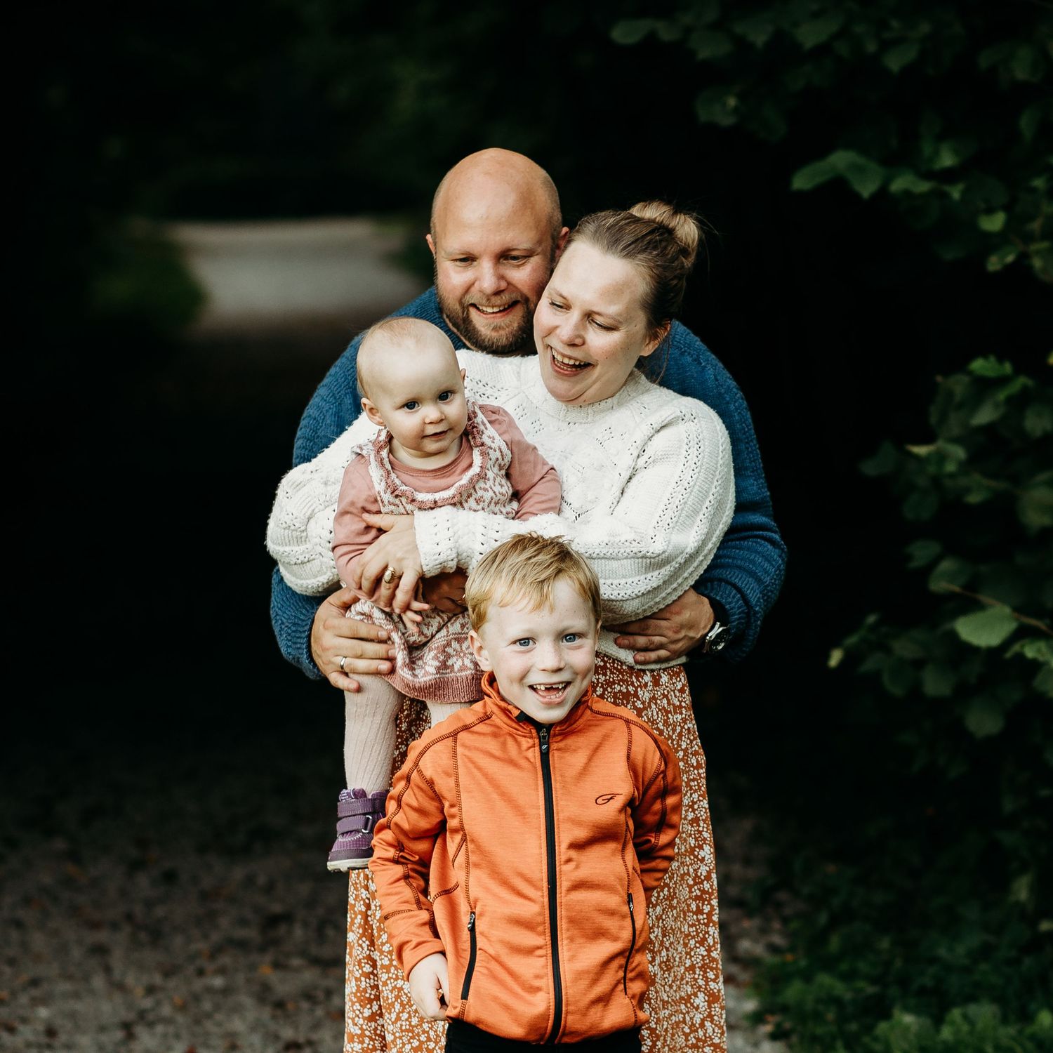 Familiefotograf Moss: En lykkelig familie som ler og klemmer hverandre i en stemningsfull skog i Østfold under en utendørs fotografering.