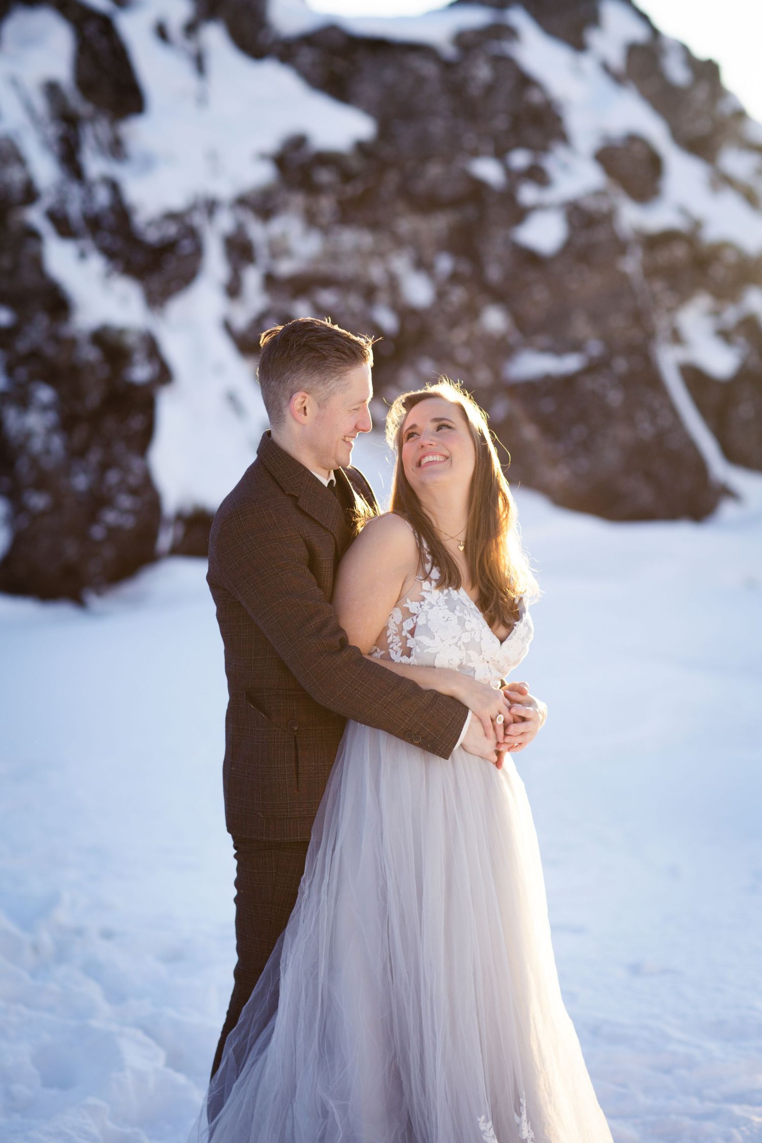 Romantic winter wedding photoshoot with couple embracing in snowy landscape.